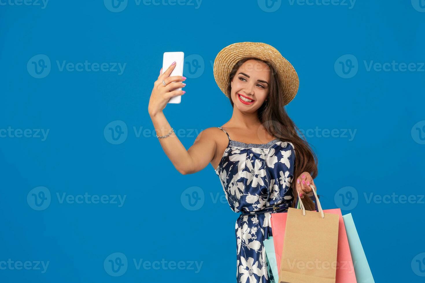 ung eleganta kvinna Framställ och tar en selfie på de telefon med handla påsar på en blå bakgrund foto