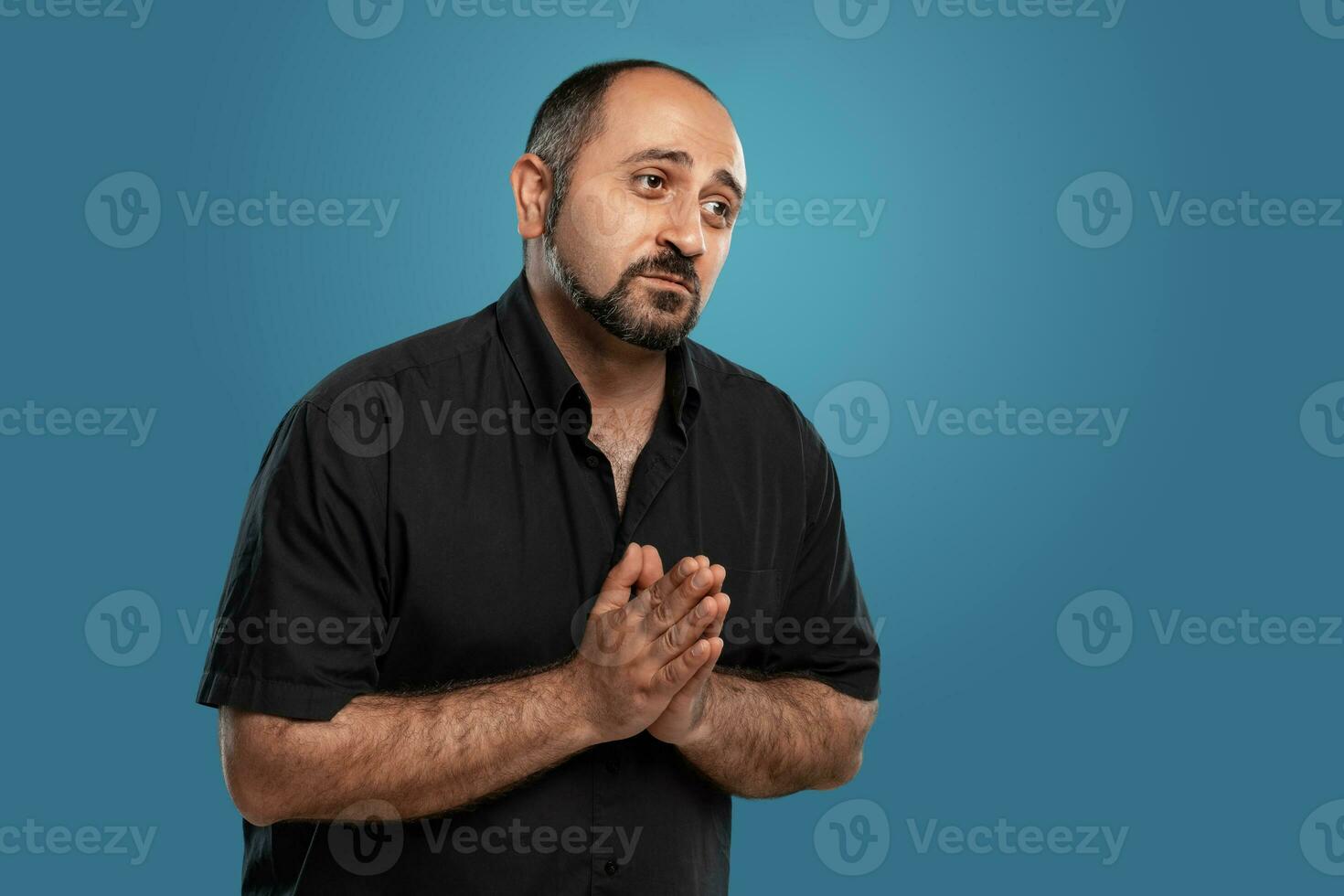 närbild porträtt av en brunett medelålders man med skägg, klädd i en svart t-shirt och Framställ mot en blå bakgrund. foto
