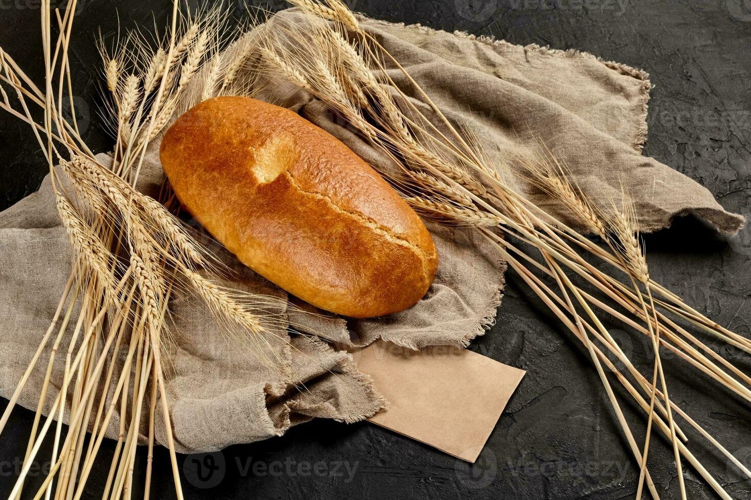 vete bröd limpa på grov säckväv med öron av vete på svart bakgrund foto