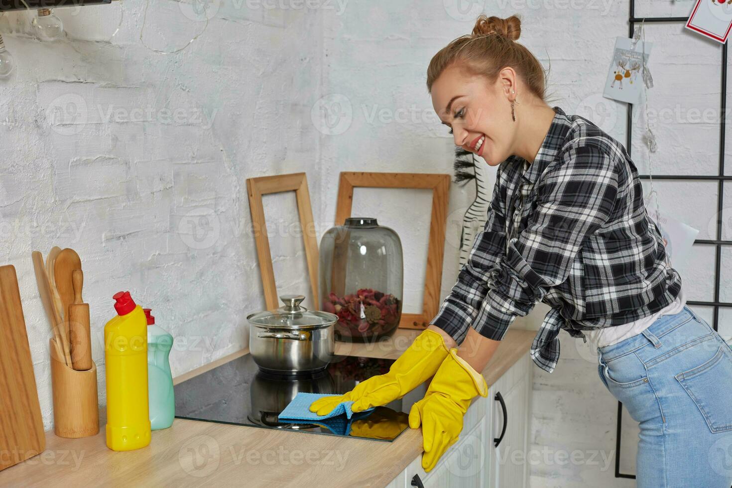 blond kvinna i skyddande handskar med trasa rengöring elektrisk spis på Hem kök. flicka tvättning svart skinande yta av kök topp foto