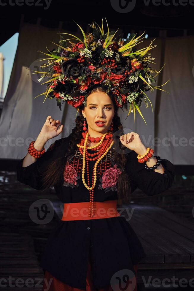 brunett flicka i en vit ukrainska äkta nationell kostym och en krans av blommor är Framställ mot en terrass. närbild. foto