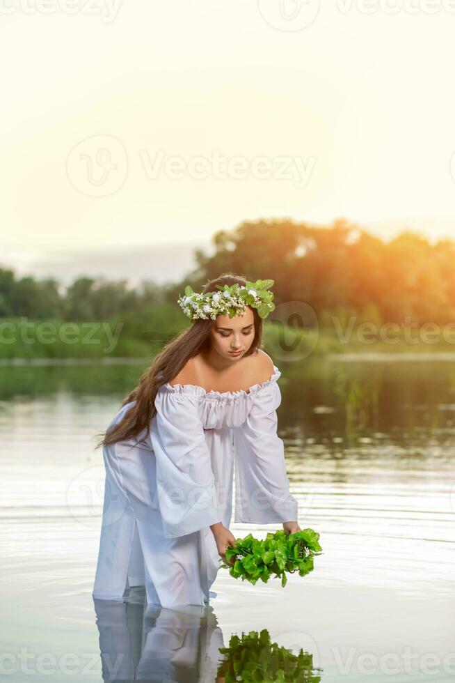 kvinna i vit klänning i de vatten. konst kvinna med krans på henne huvud i flod. krans på henne huvud, slavic traditioner och hedendom foto