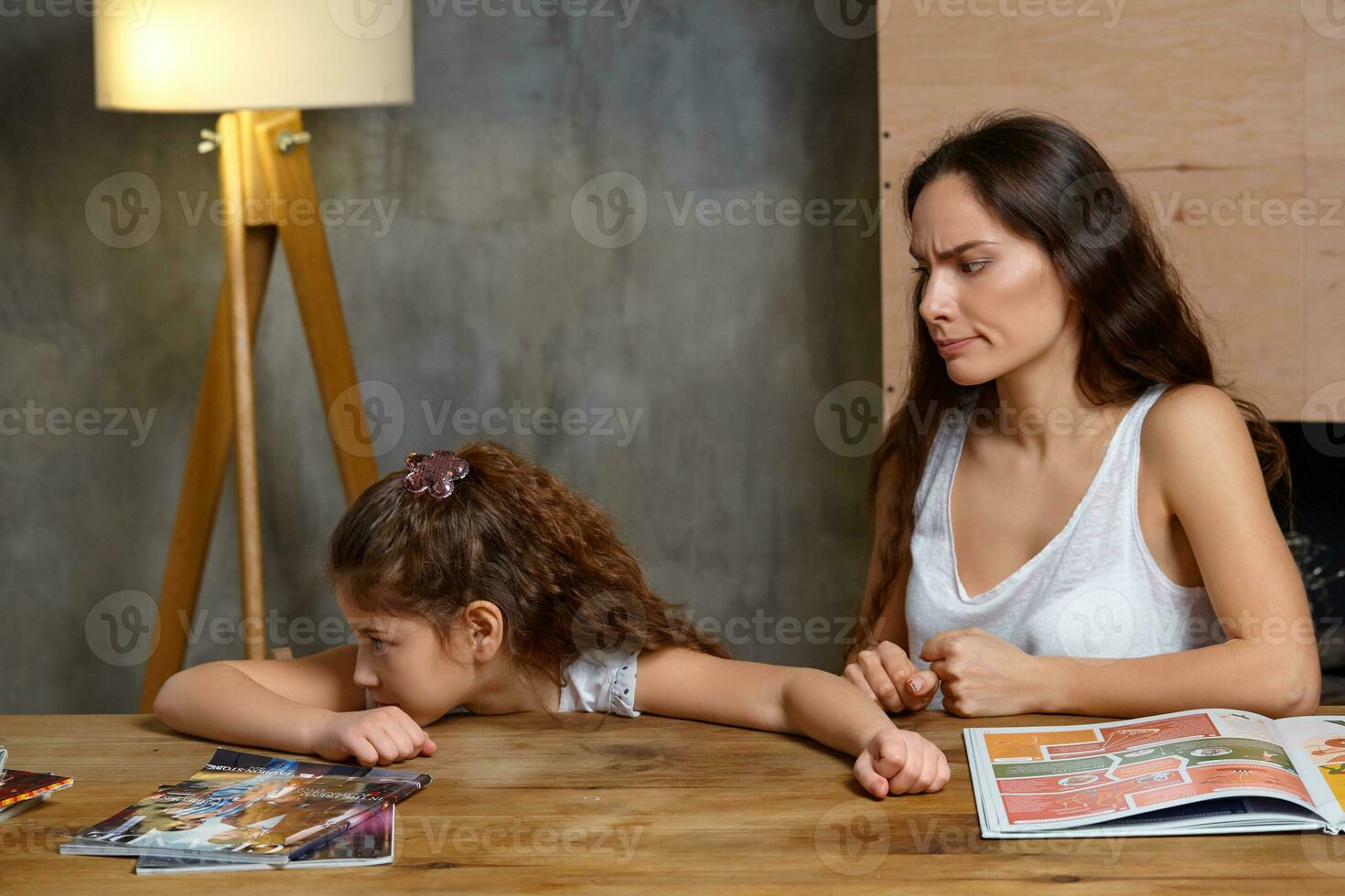 porträtt av en mor portion henne små ljuv och söt dotter till göra henne läxa inomhus. Lycklig familj. foto
