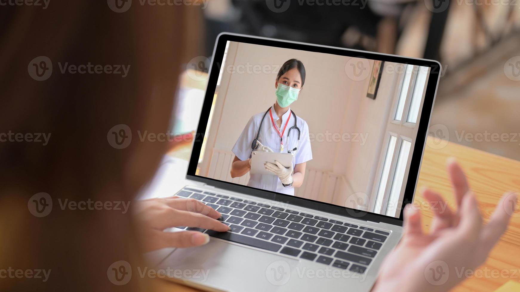 sjuk kvinna använder ett videosamtal från en bärbar dator för att få råd från en läkare, hålla en surfplatta och bära en mask. foto