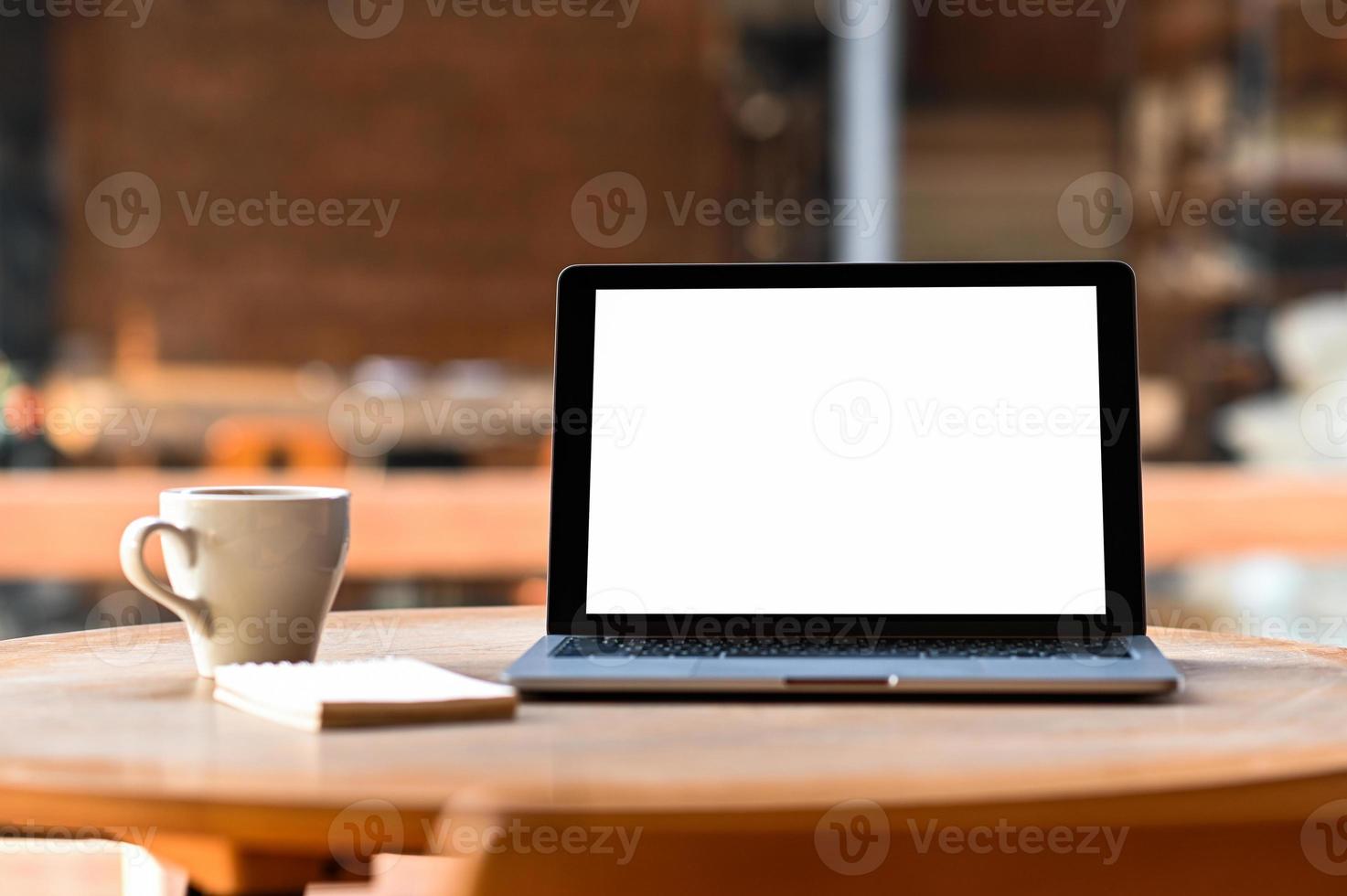 mockup tom skärm laptop med kaffe och anteckningsbok på bordet, taget framifrån. foto