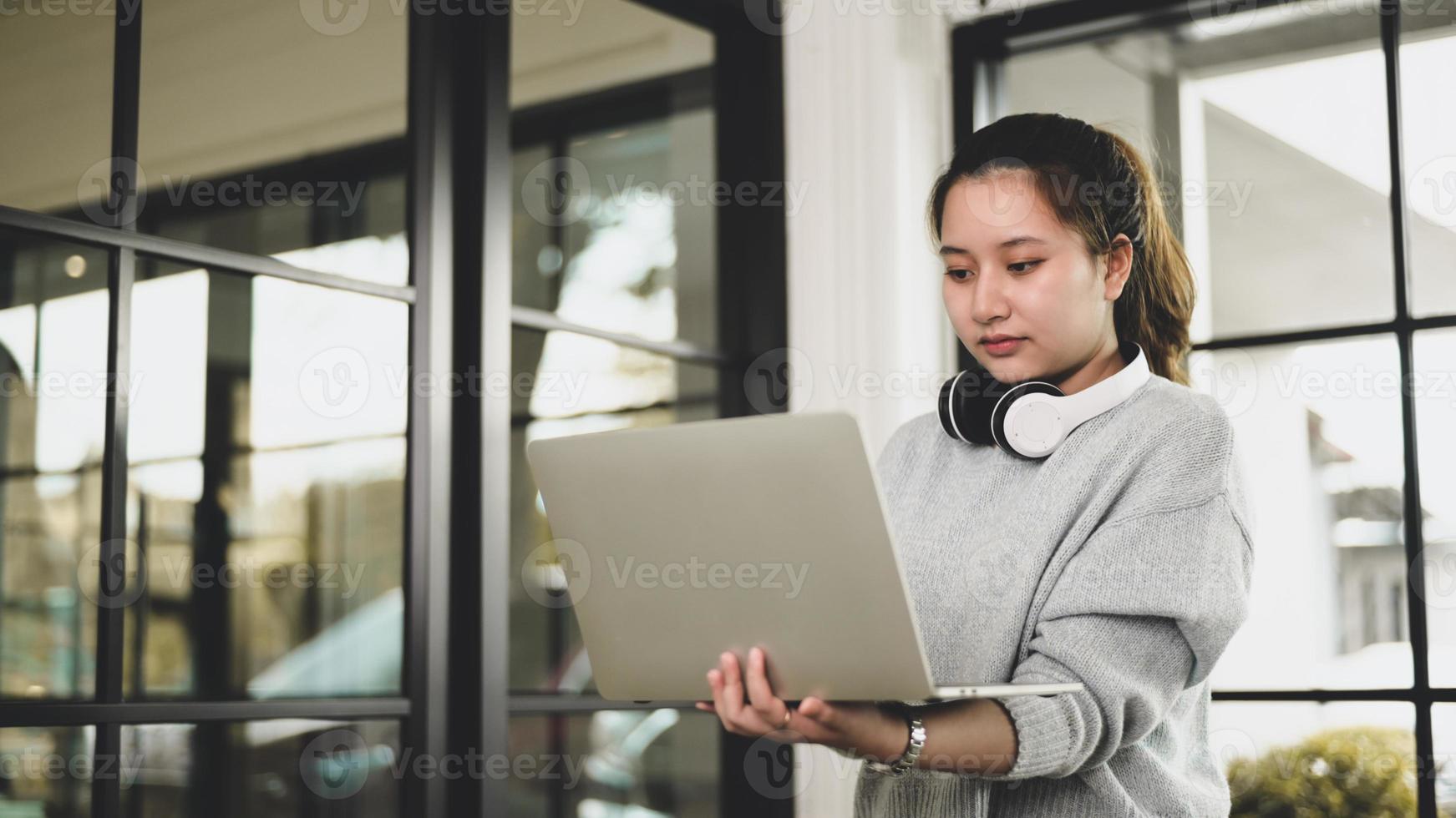 ung asiatisk tjej med hörlurar som håller laptop -videochatt med vänner. foto