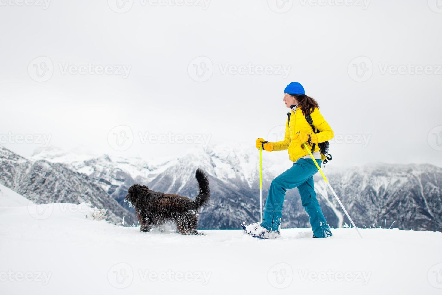 svart hund med en tjej på promenad med snöskor i bergen foto