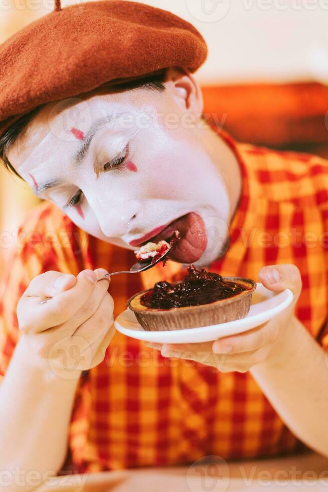 de clown är äter en kaka i en Kafé och hans ansikte är kväkande. foto