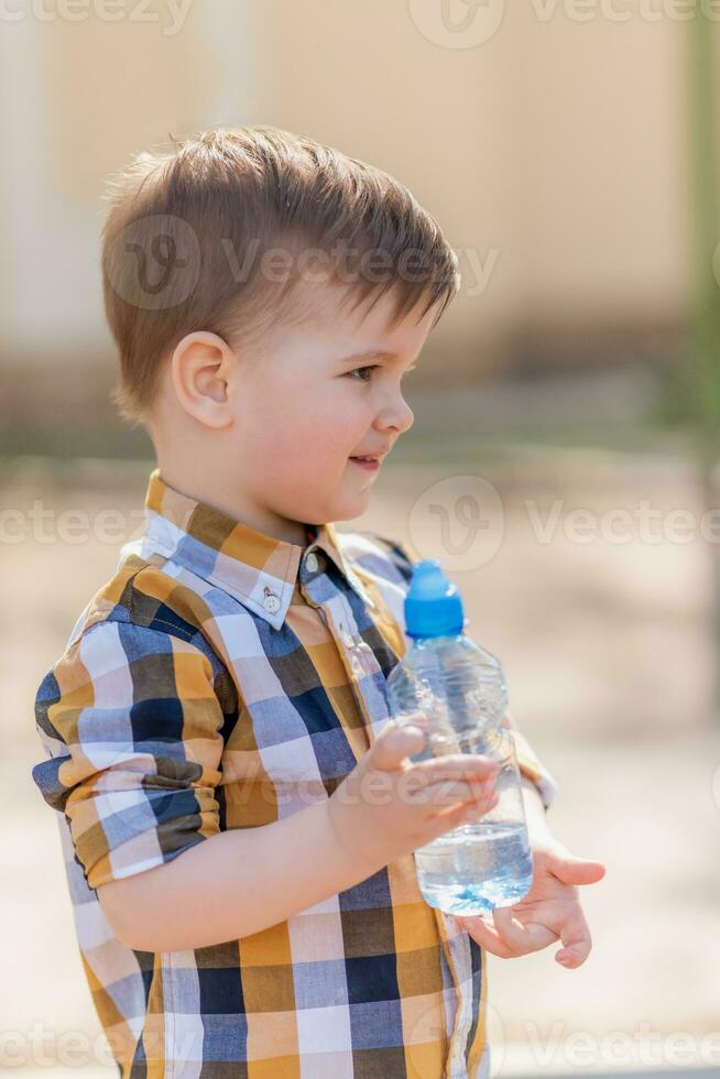 stilig pojke drycker klar vatten från en flaska på en solig dag utanför foto