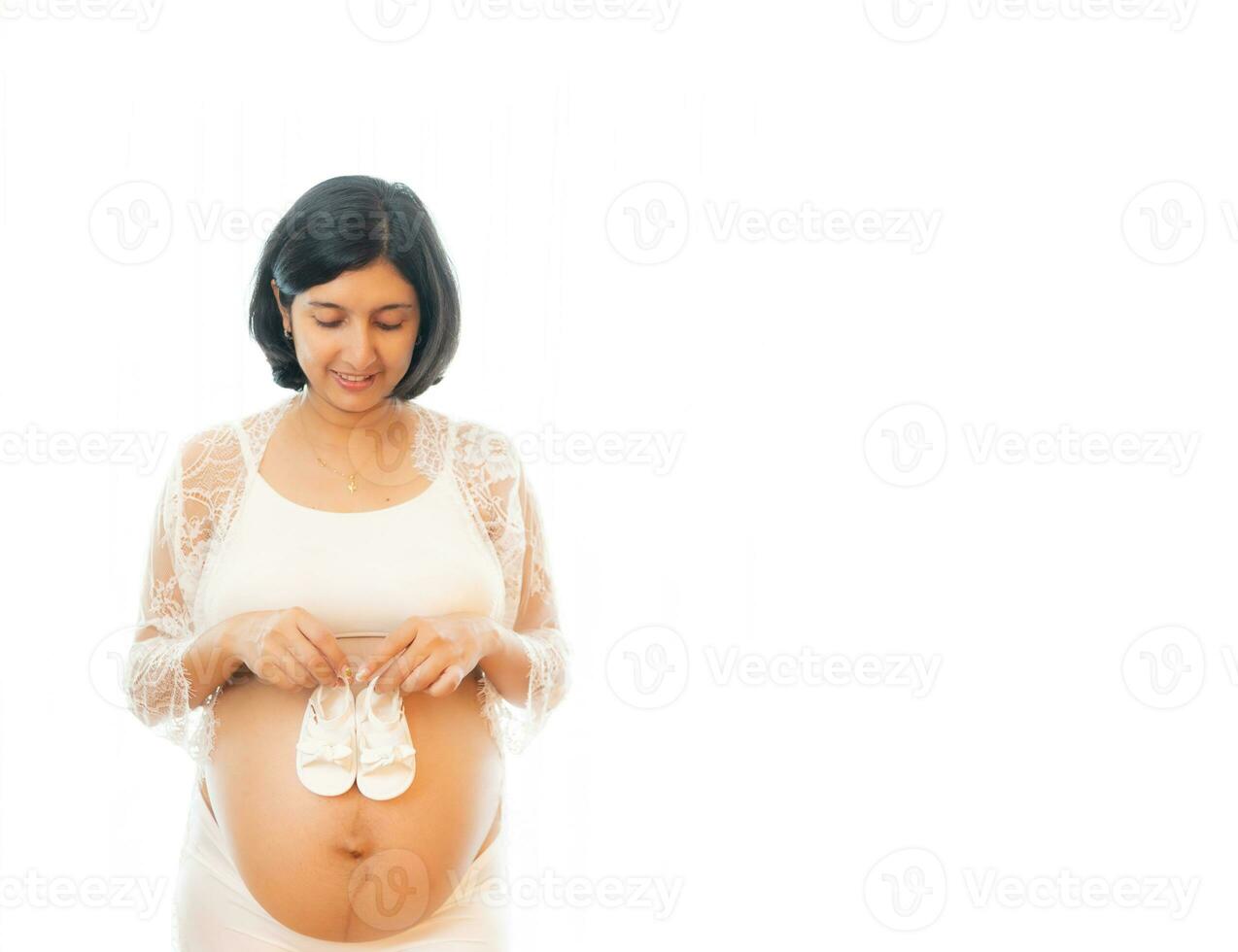 närbild gravid mage med söt mycket liten bebis skor. begrepp av graviditet, gynekologi, förberedelse. skön gravid kvinna i skjorta i vit bakgrund. kvinna innehav stor gravid mage. foto
