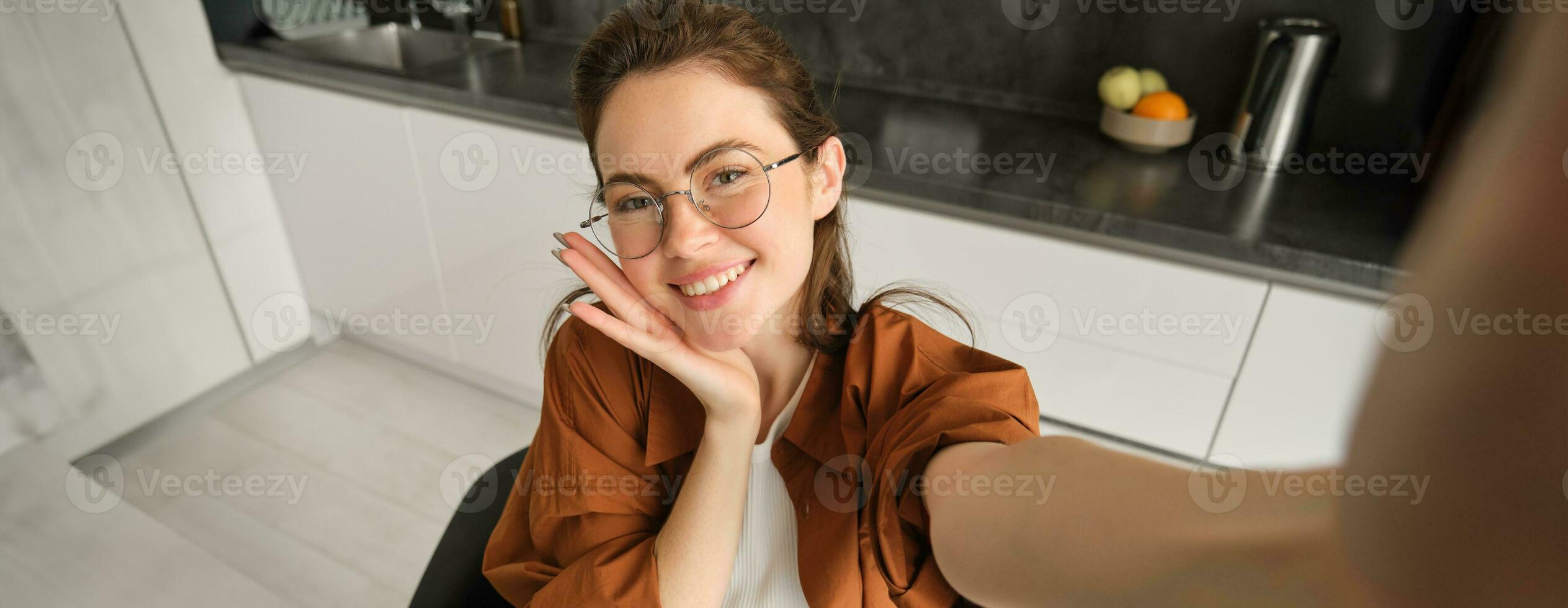 selfie av Lycklig ung och sorglös kvinna, tar Foto på mobil telefon med utökad hand, Framställ och leende, Sammanträde i kök i glasögon