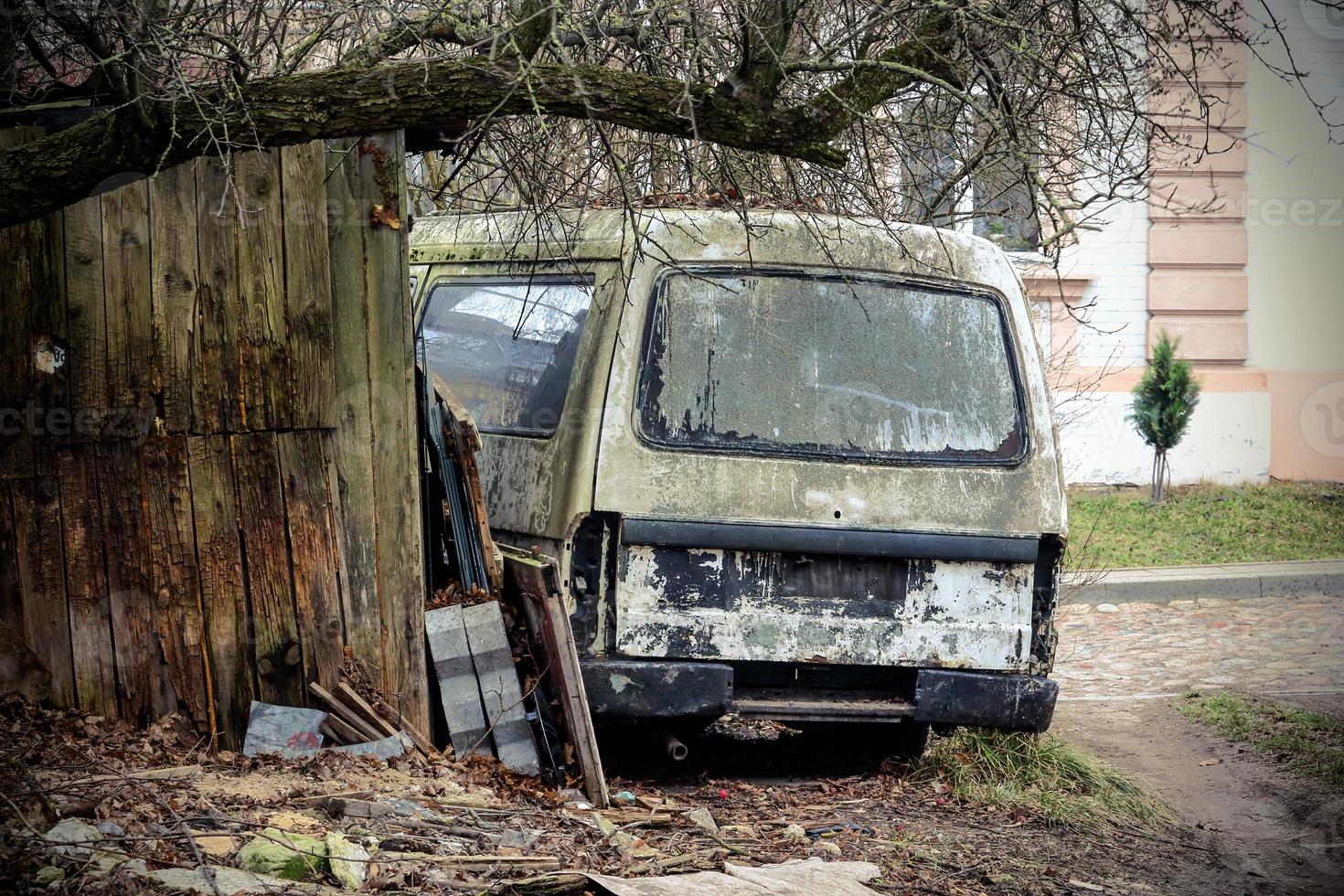 gammal trasig rostig skåpbil nära träbyggnad under lövlöst träd foto