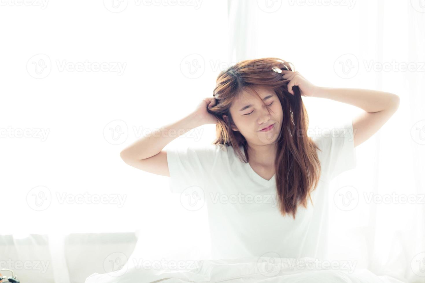 ung asiatisk kvinna stretch och slappna av i sängen efter att ha vaknat på morgonen i sovrummet. foto