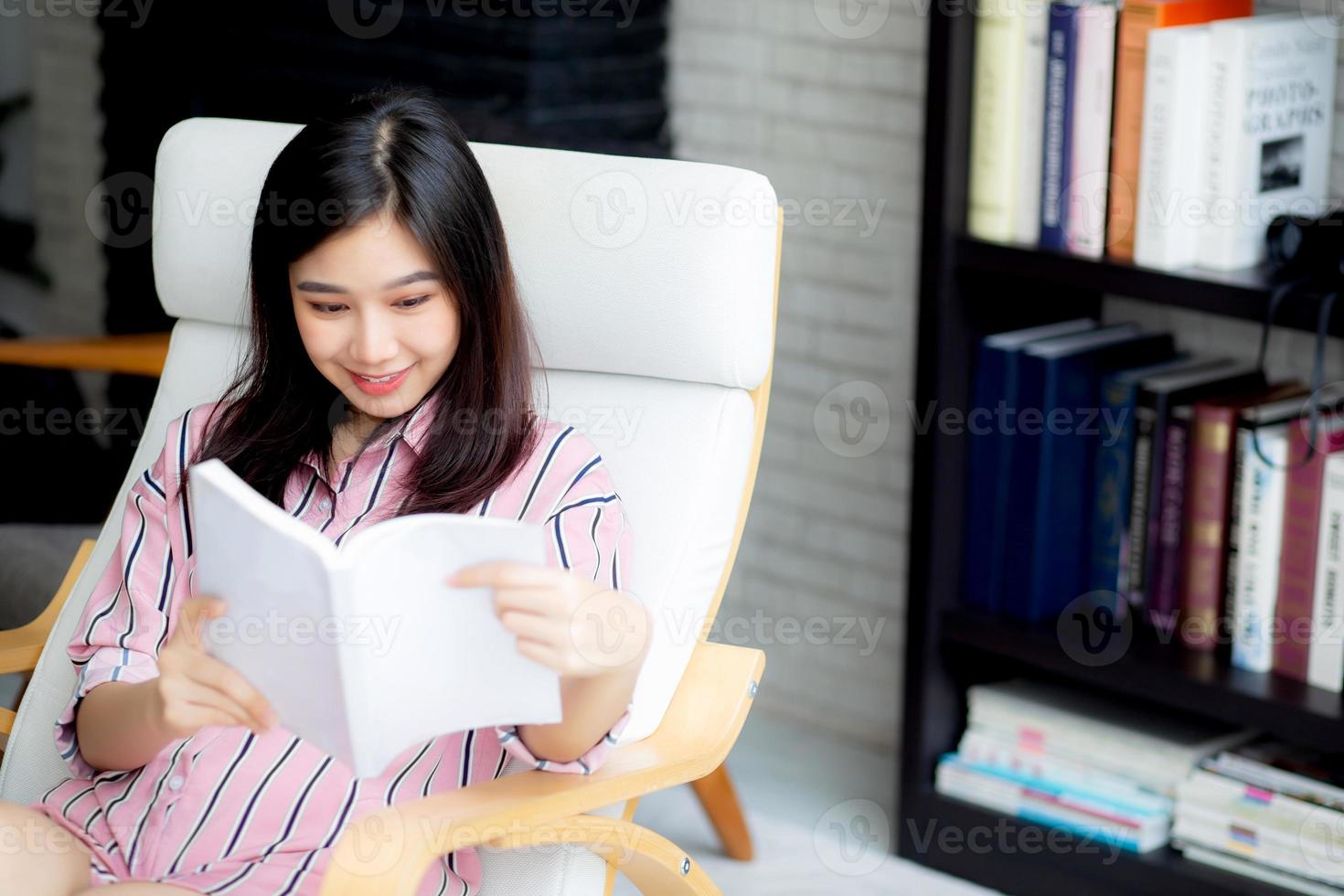 ung asiatisk kvinna koppla av sittande läsbok i vardagsrummet. foto