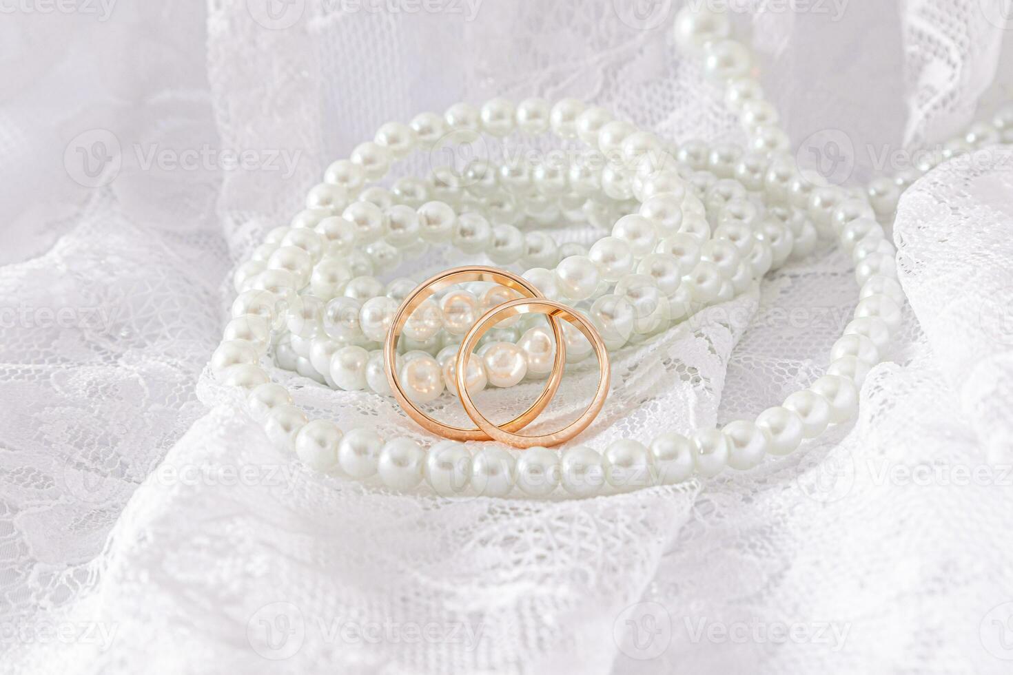 retro beige tyll och lång pärla pärlor hänga längs de mjuk veck av tyg med guld bröllop ringar. en kopia Plats. attrapp foto