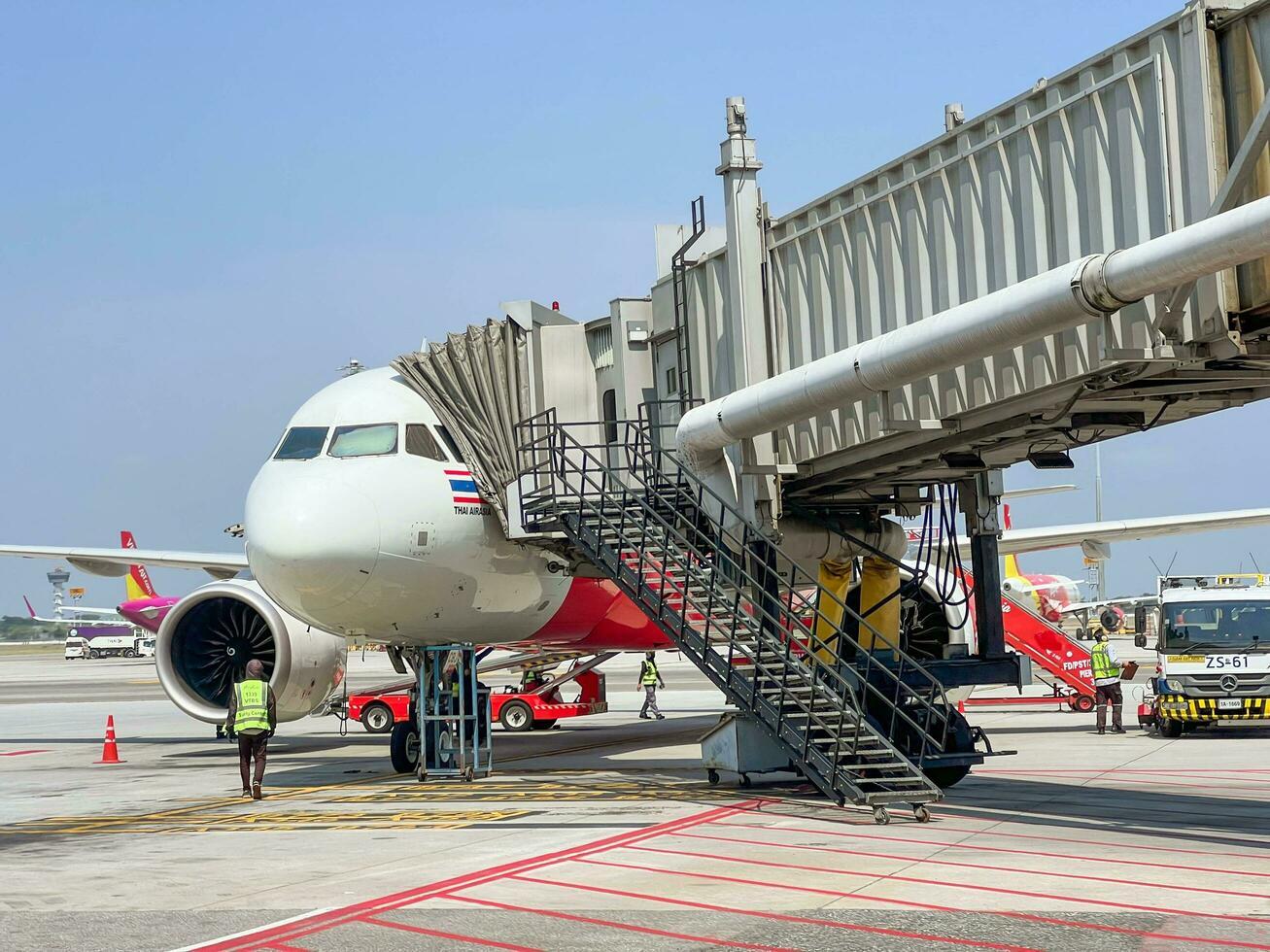 Bangkok, th, 2022 - se av utanför terminal suvarnabhumi internationell flygplats med thai flygplan ankommer och parkerad levererar passagerare med jet bro under ljus blå himmel. foto