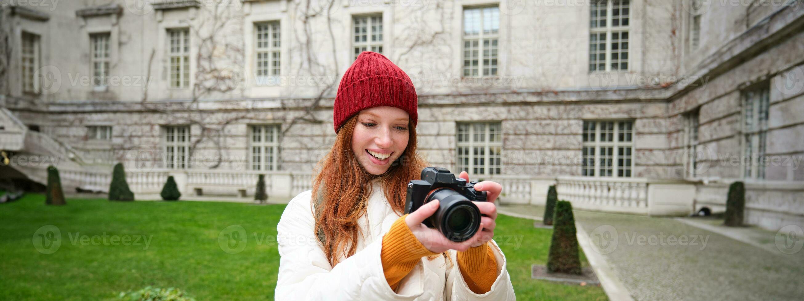 Lycklig rödhårig flicka turist, tar foton, fotograf med professionell kamera promenader runt om stad och fångar skön bilder foto