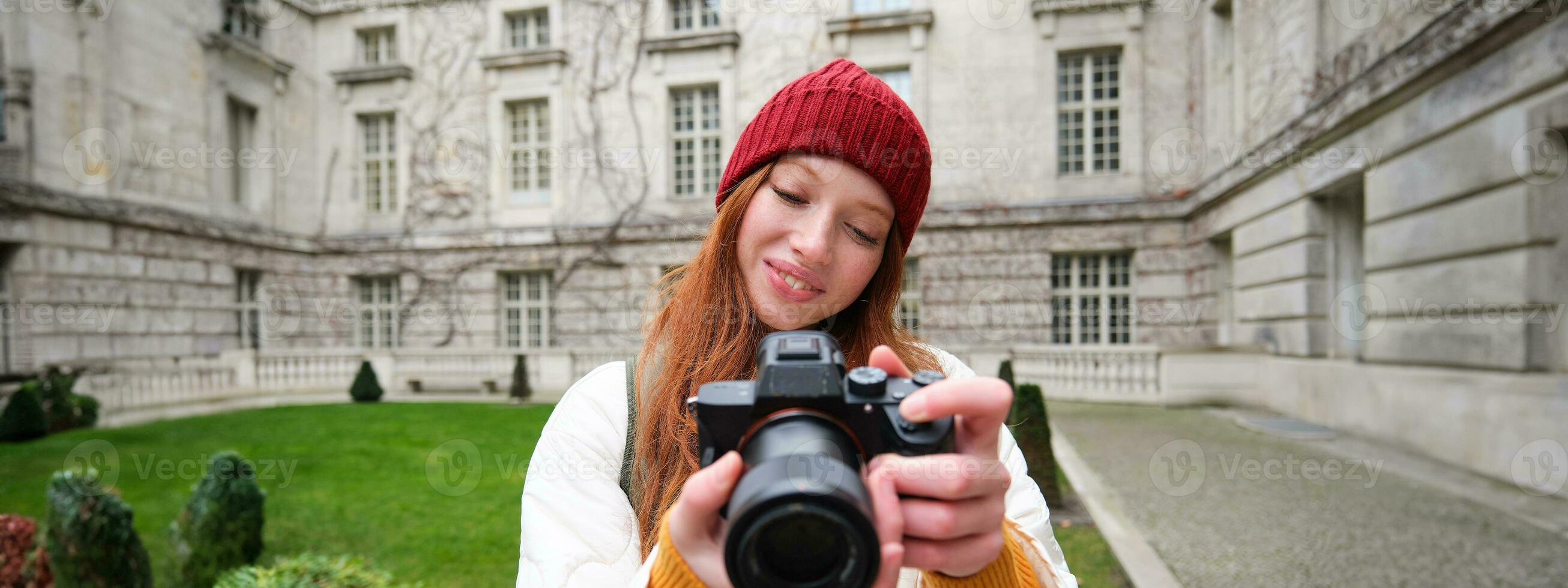 Lycklig rödhårig flicka turist, tar foton, fotograf med professionell kamera promenader runt om stad och fångar skön bilder foto