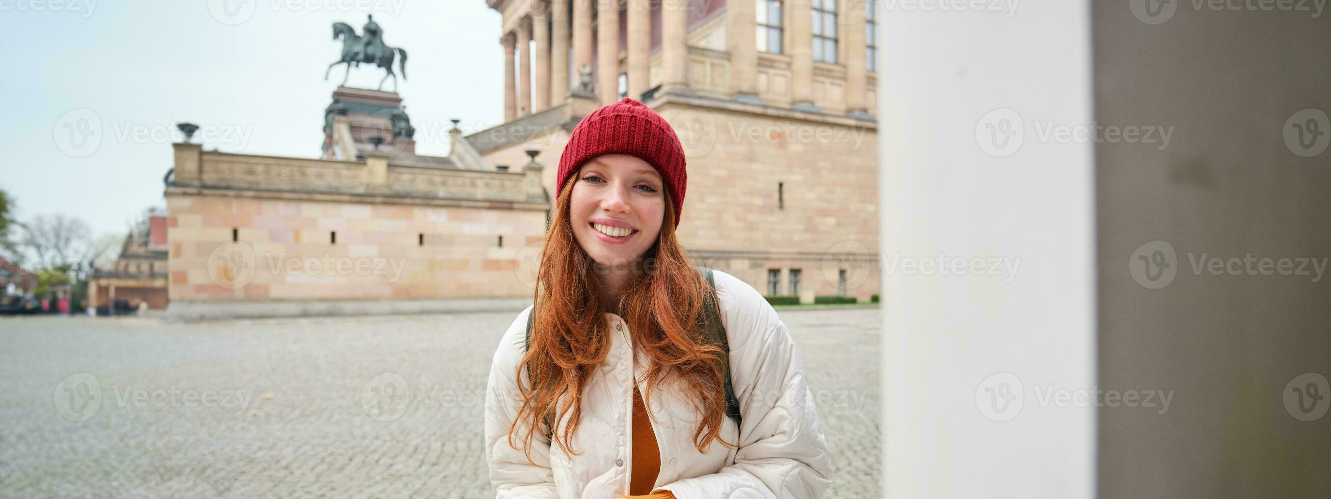 leende rödhårig flicka turist, promenader runt om stad och utforskar populär landmärken, sightseeing, innehav smartphone, ser på henne mobil app och checkar med stad Karta foto
