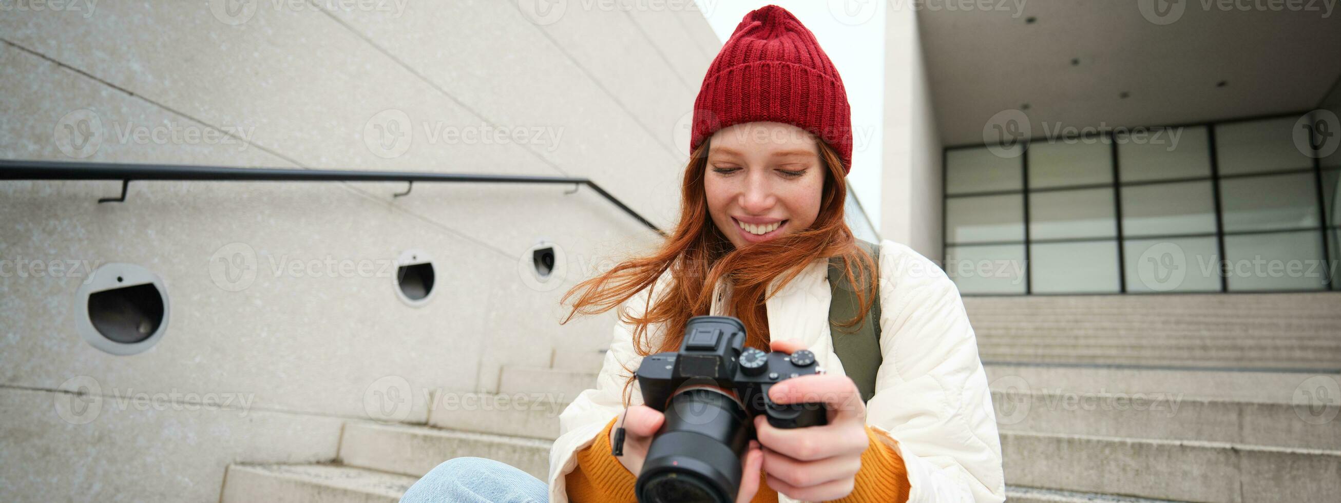 urban människor och livsstil. Lycklig rödhårig kvinna tar foton, innehav professionell digital kamera, fotografering på gator foto