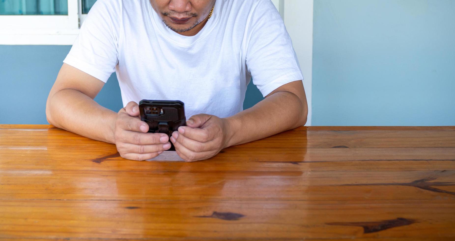 asiatisk man som bär vit skjorta med telefonen på ett träbord foto