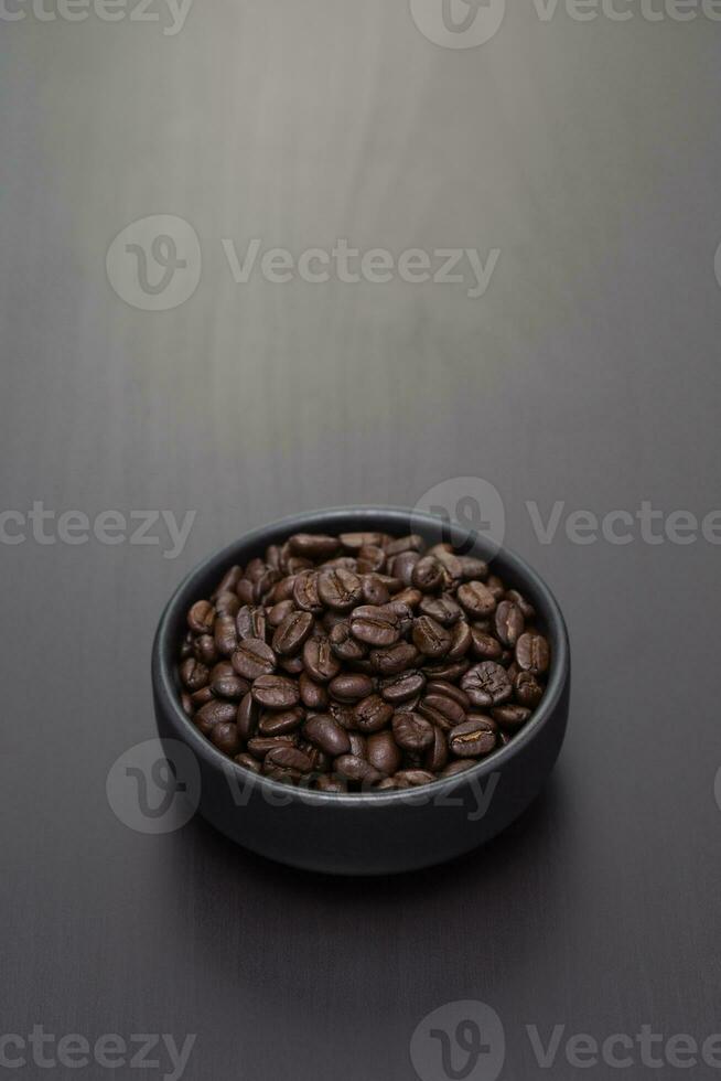 mörk rostad kaffe bönor i en små svart keramisk skål. foto