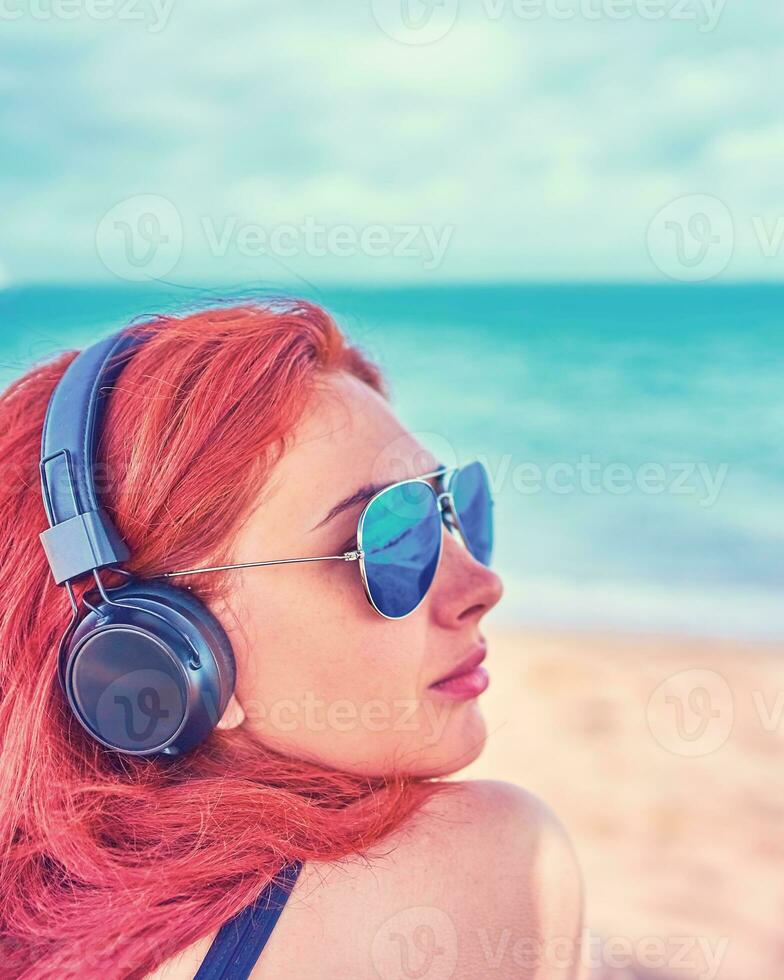 Häftigt kvinna lyssnande till musik på de strand. de flicka åtnjuter en skön se av de hav och lyssnar till musik. foto