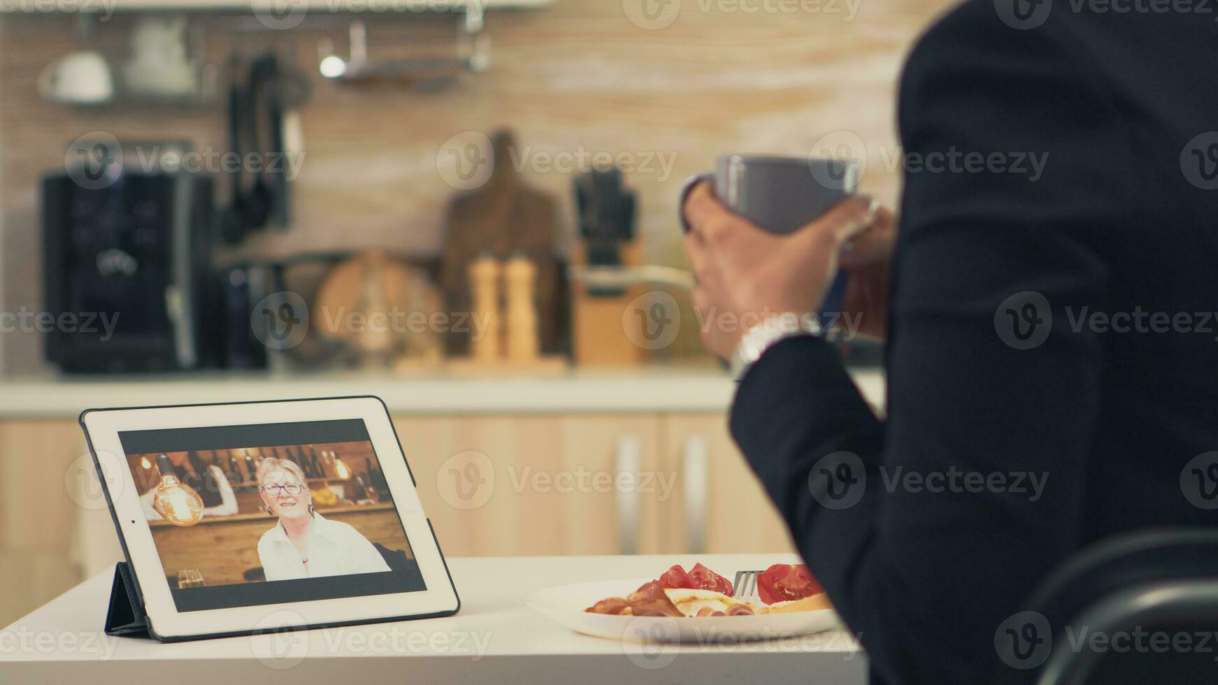 företag kvinna på en video ring upp med henne mor under frukost. använder sig av modern uppkopplad internet webb teknologi till chatt via webbkamera videokonferens app med släktingar, familj, vänner och medarbetare foto