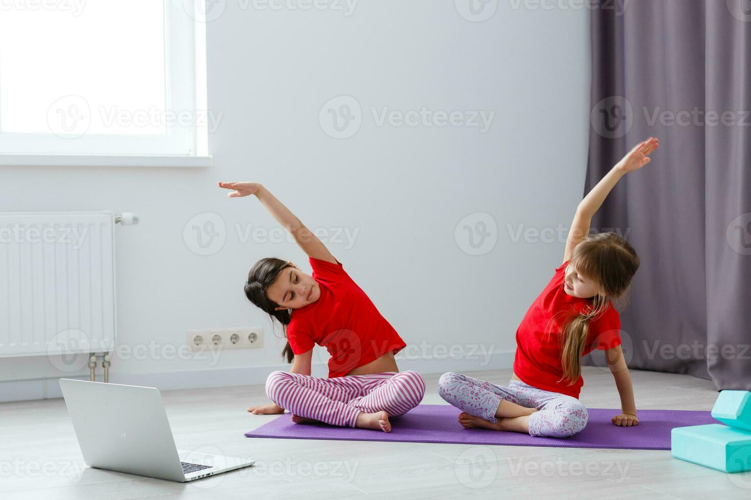 två liten flickor praktiserande yoga, stretching, kondition förbi video på anteckningsbok. avlägsen uppkopplad utbildning Träning, aerob på Hem. friska livsstil, coronavirus, stanna kvar Hem. barn sport Hem karantän. foto