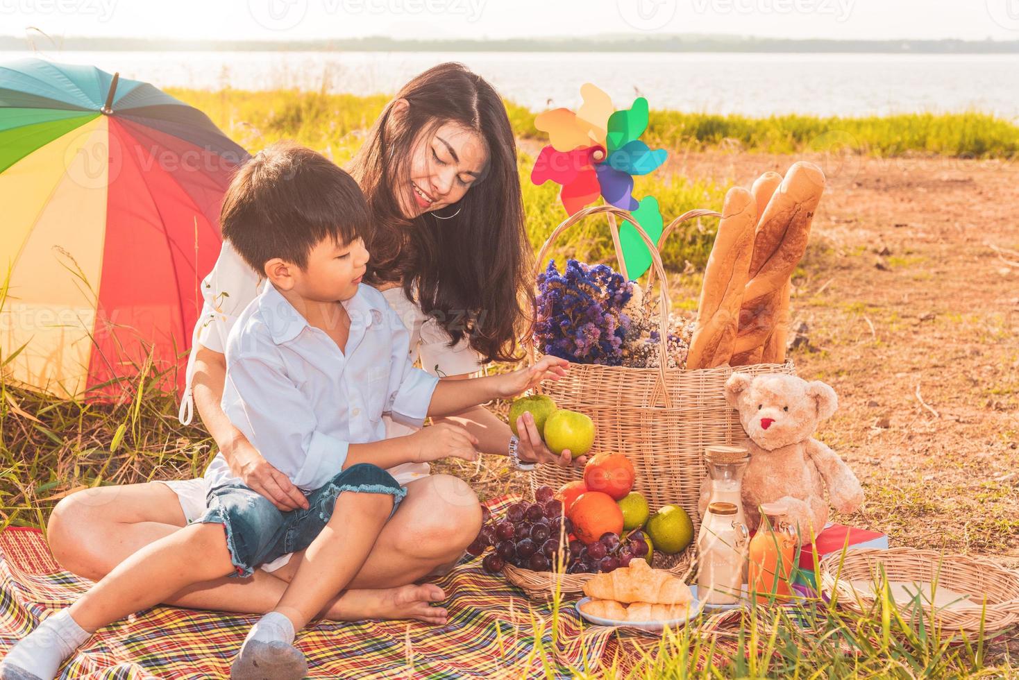 vacker asiatisk mamma och son gör picknick och i påsk sommarfest på äng nära sjö och berg. semester och semester. människors livsstil och lyckligt familjelivskoncept. thailändsk person foto