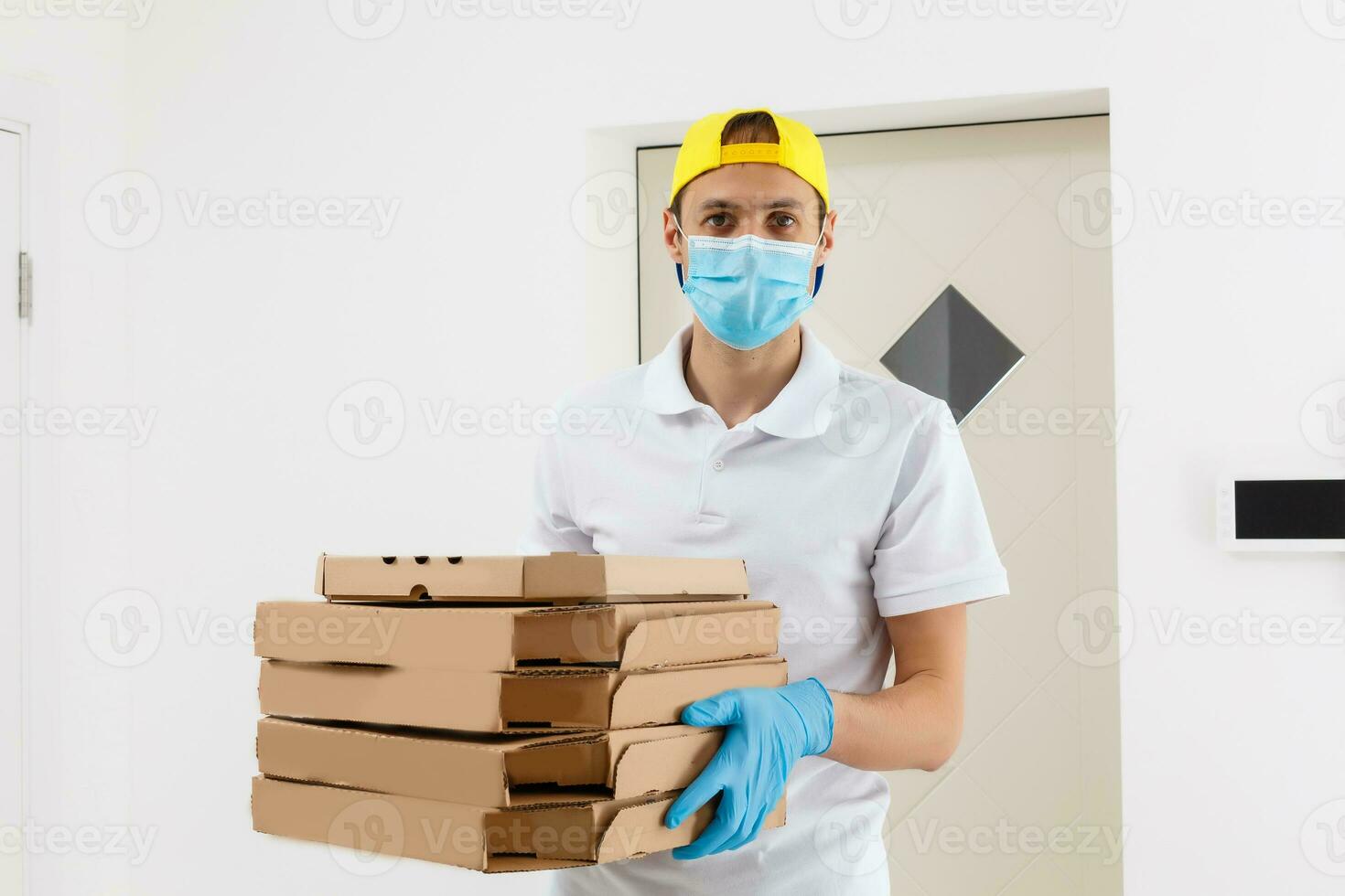 man från leverans service i t-shirt, i skyddande mask och handskar ger mat beställa och innehav pizza lådor över vit bakgrund foto