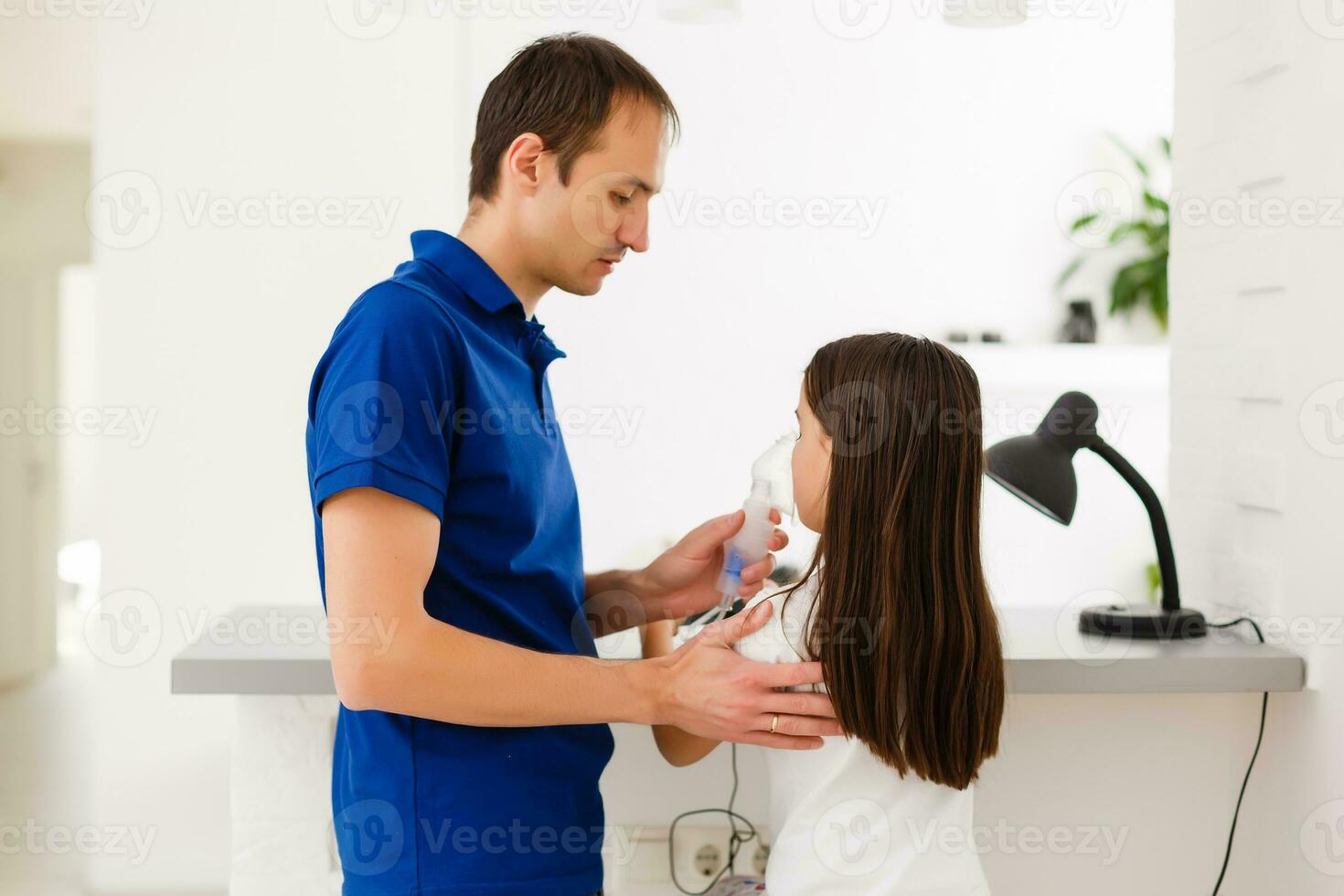 liten litet barn flicka framställning inandning med nebulisator på Hem. far portion och innehav de enhet. barn har influensa, hosta och bronkit. astma inhalator inandning ånga sjuk begrepp foto