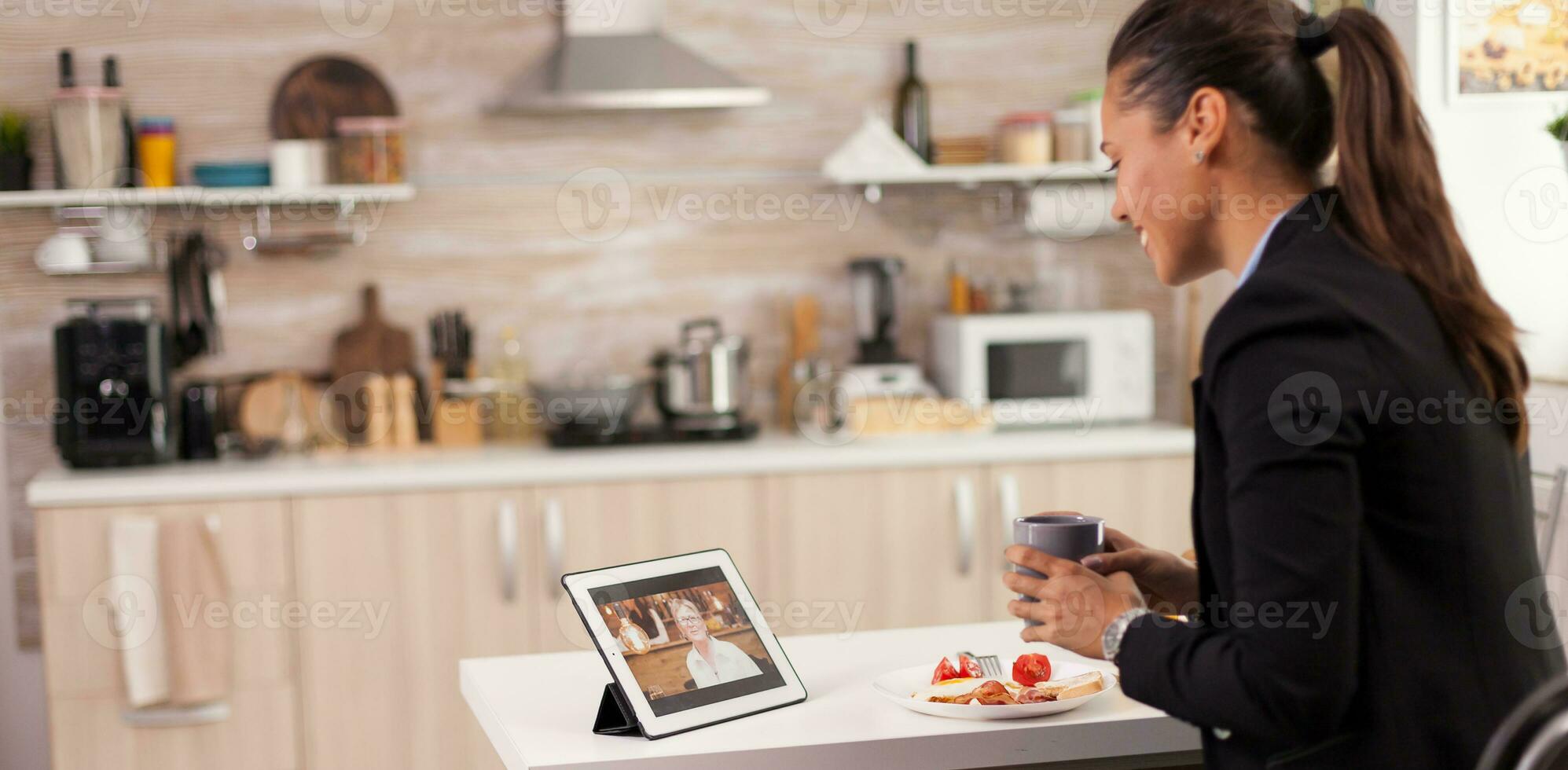 företag kvinna på en video ring upp med henne mor under frukost. använder sig av modern uppkopplad internet webb teknologi till chatt via webbkamera videokonferens app med släktingar, familj, vänner och medarbetare foto