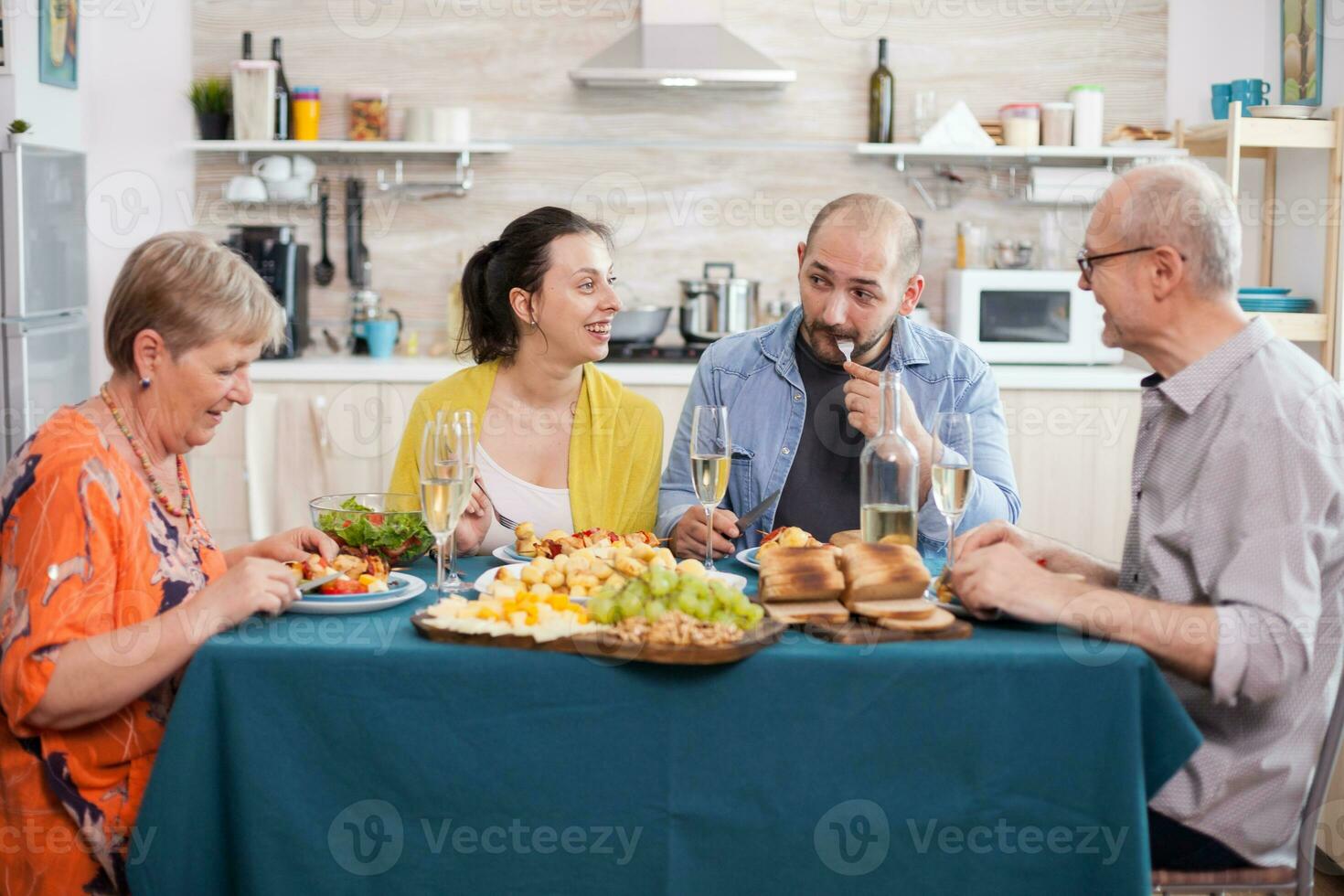 dotter leende på far i kök under familj lunch. man äter utsökt mat. Lycklig senior man på dining tabell. gott rostad potatisar. foto