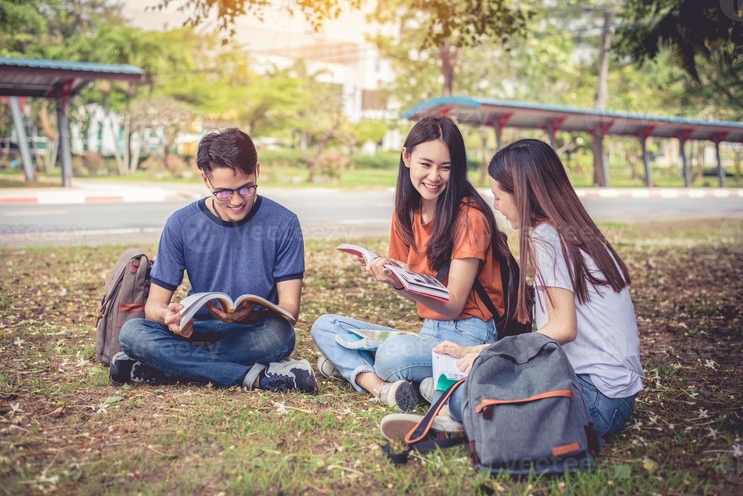 grupp asiatiska högskolestudenter som läser böcker och undervisar specialklass för tentamen på gräsplan utomhus. lycka och utbildning inlärningskoncept. tillbaka till skolan koncept. tonåring och människor tema foto