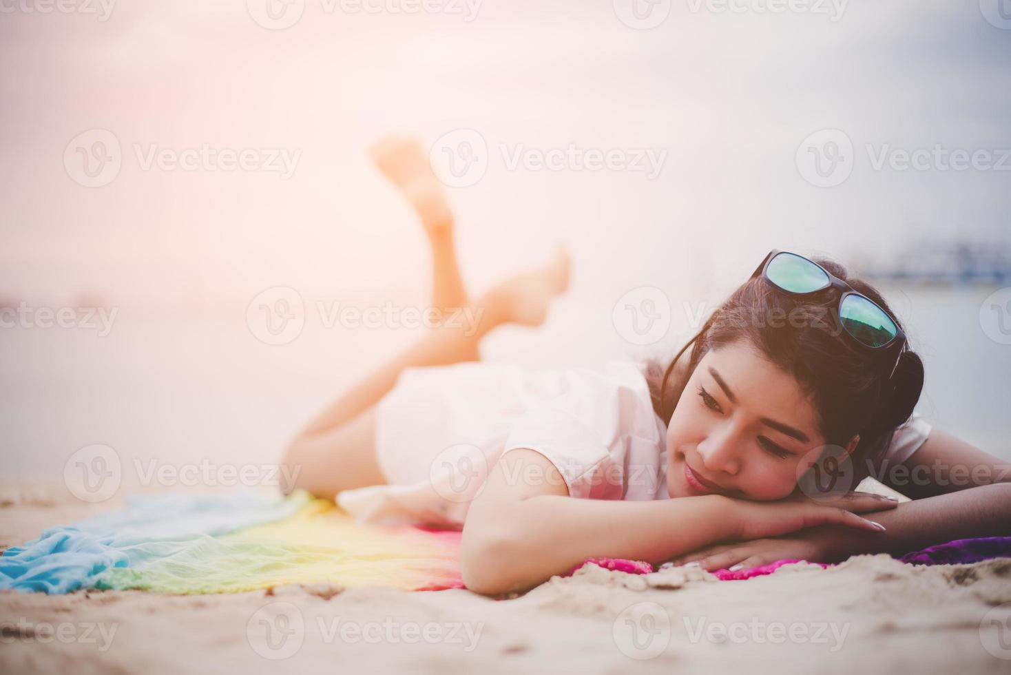 skönhet asiatisk kvinna har semester på stranden. flicka som bär solglasögon och ligger på färgglad matta nära havet. livsstil och lyckligt liv koncept. resa och semester tema. sommar och tropiskt tema foto