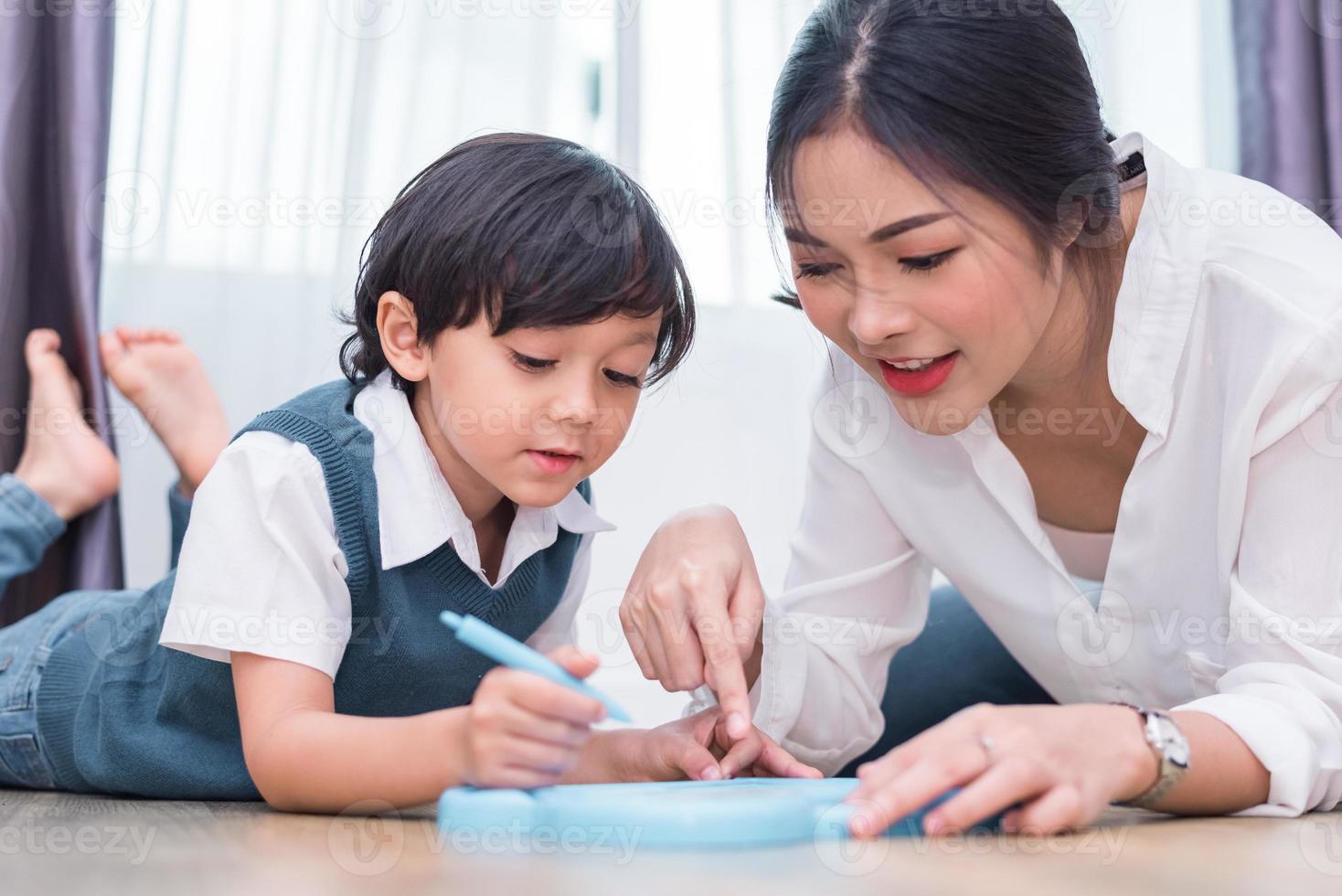 asiatisk mamma som lär söt pojke att rita rött hjärta ombord med färgpenna. tillbaka till skolan och utbildning koncept. familj och hem söt hem tema. tema för förskolebarn. sikt framifrån foto