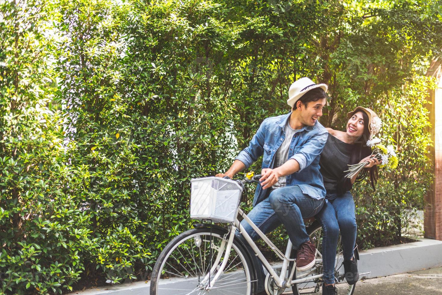 lyckligt par som cyklar tillsammans i romantisk utsikt park bakgrund. alla hjärtans dag och bröllop smekmånad koncept. människor och livsstil koncept foto