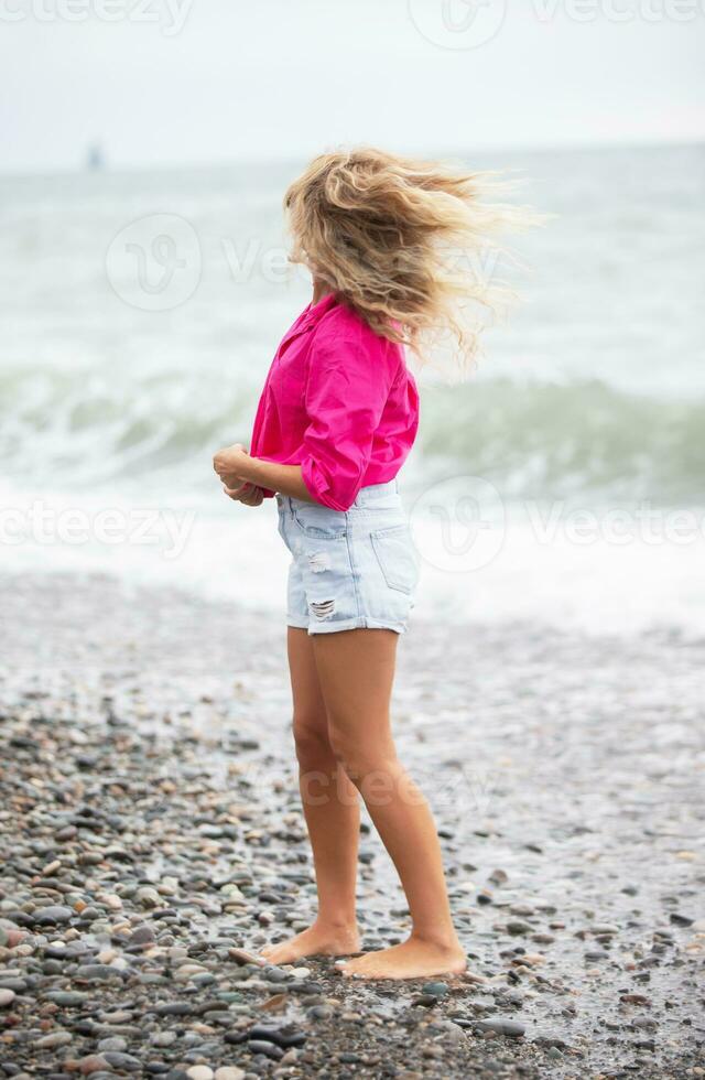 skön kvinna på de bakgrund av de hav i denim shorts och en ljus skjorta. foto