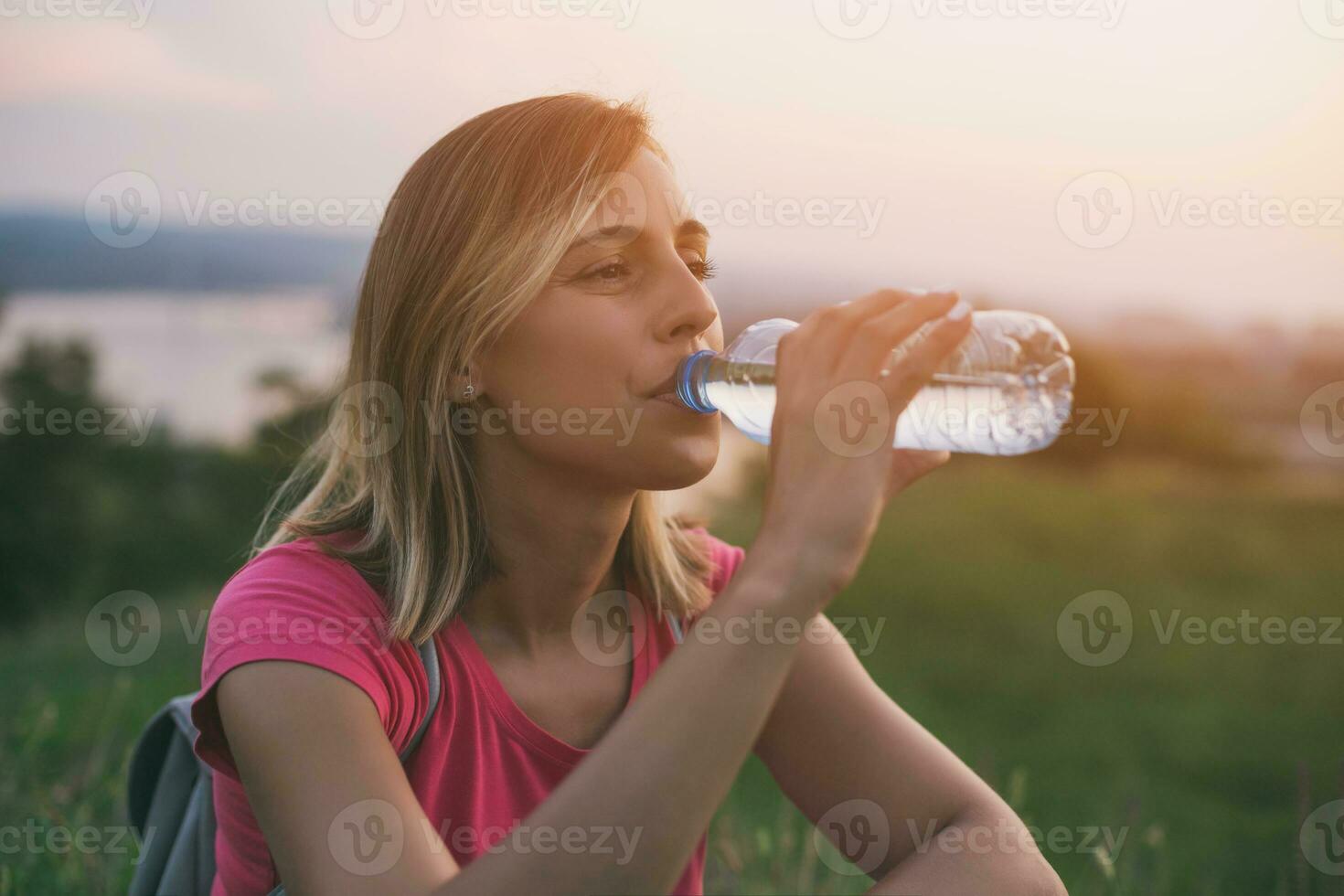 skön kvinna åtnjuter dricka vatten utomhus- med en stadsbild och flod se Bakom hennes.tonade bild. foto