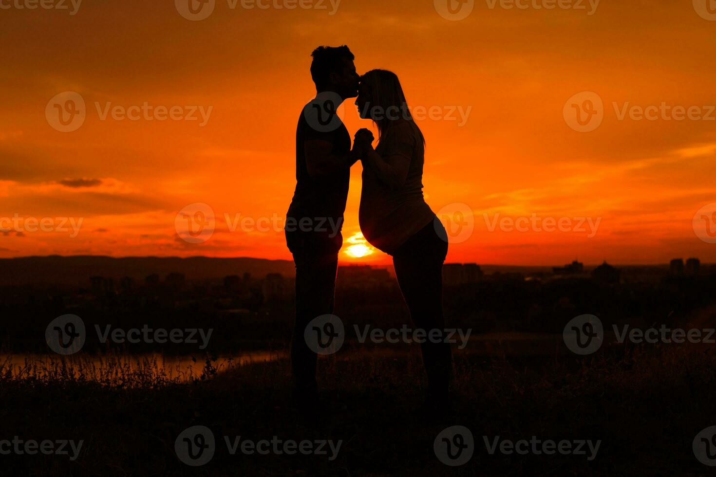silhuetter av Make kissing hans gravid fru in i panna och njut av utgifterna tid tillsammans utomhus.tonad bild. foto