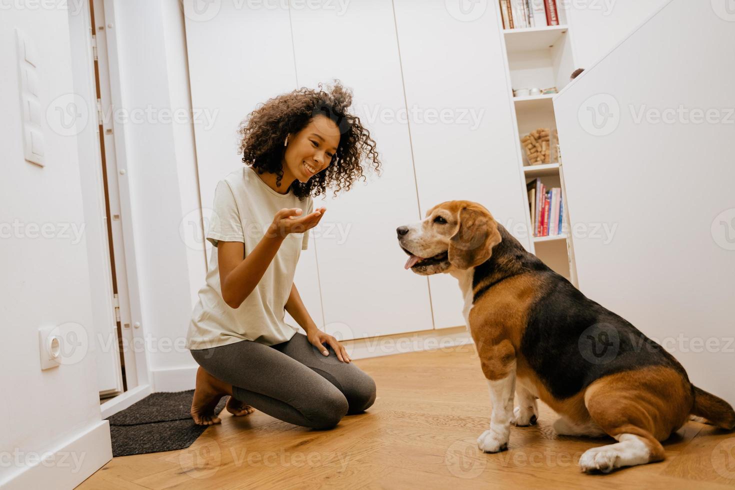 svart ung kvinna i hörlurar leende medan hon matar sin hund foto