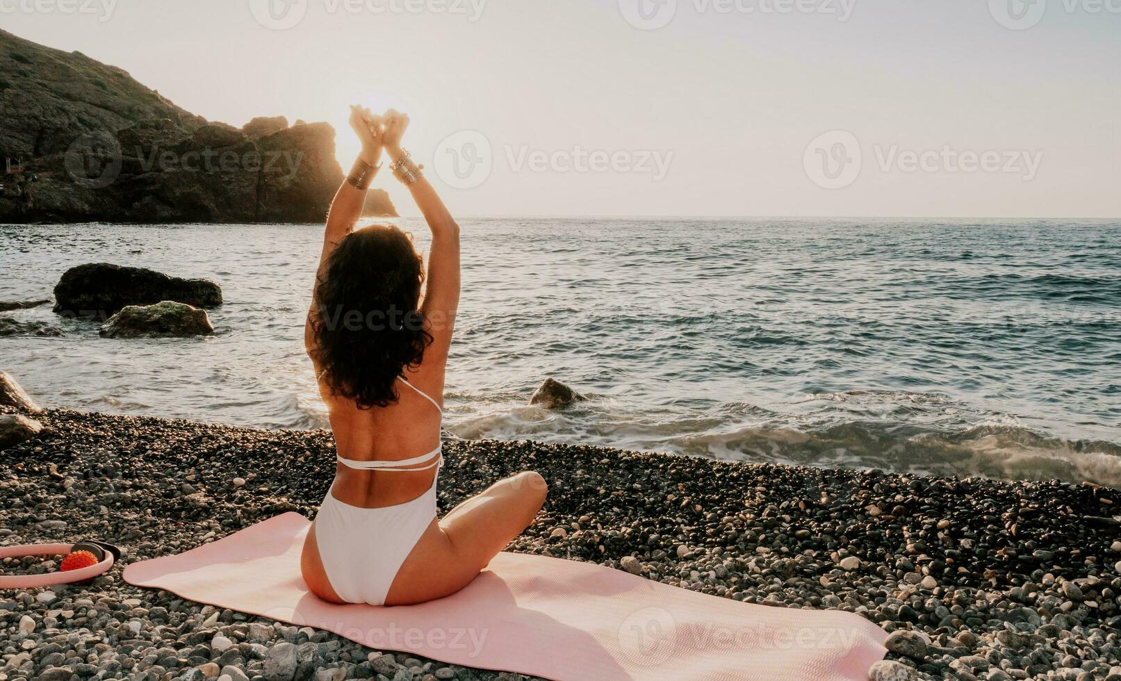 kvinna hav yoga. Lycklig kvinna i vit baddräkt och boho stil armband praktiserande utomhus på yoga matta förbi hav på solnedgång. kvinnor yoga kondition rutin. friska livsstil, harmoni och meditation foto