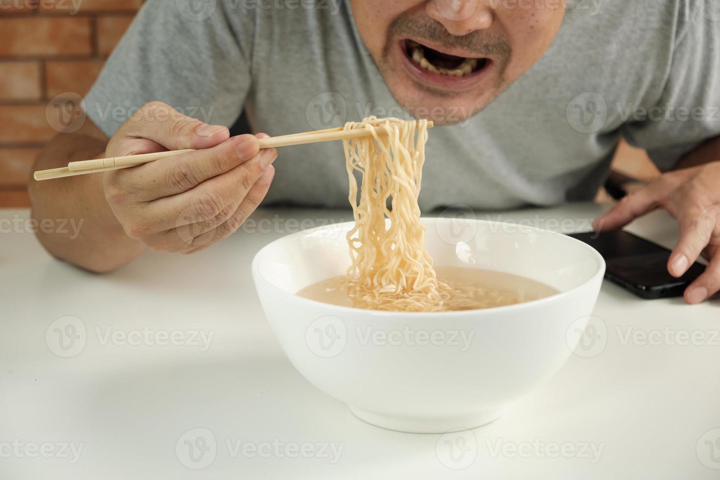 hungrig avslappnad thailändsk man använder ätpinnar för att äta varma snabbnudlar i vit kopp under lunchpauser, snabb, god och billig. traditionell hälsosam asiatisk snabbmatsmåltid av japansk och kinesisk livsstil. foto