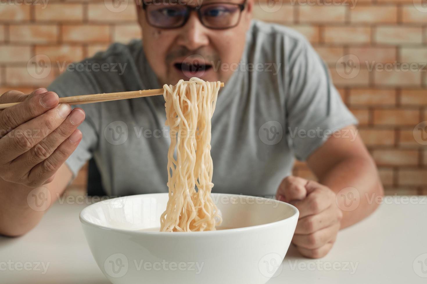 hungrig avslappnad thailändsk man på tegelväggsbakgrunden använder ätpinnar för att äta varma snabbnudlar i vit kopp under lunchpauser, snabb, god och billig. traditionell asiatisk snabbmatskök livsstil. foto