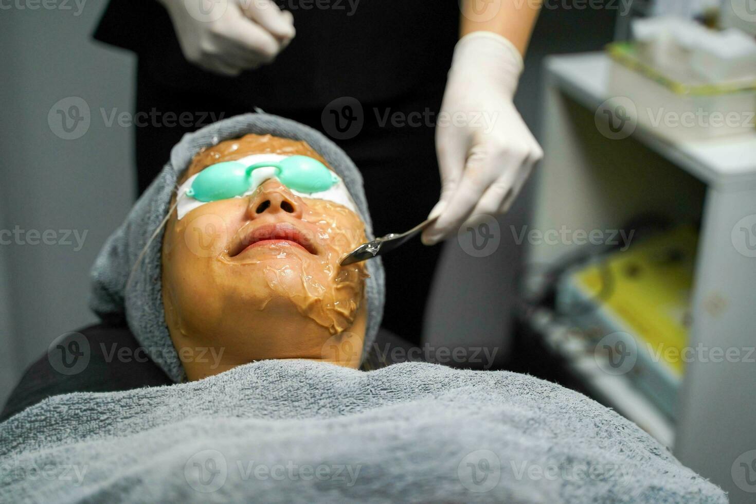 närbild asiatisk skönhet kvinna tar emot hud gel till förbereda de Färg ljus terapi till stimulera ansiktsbehandling hälsa. foto