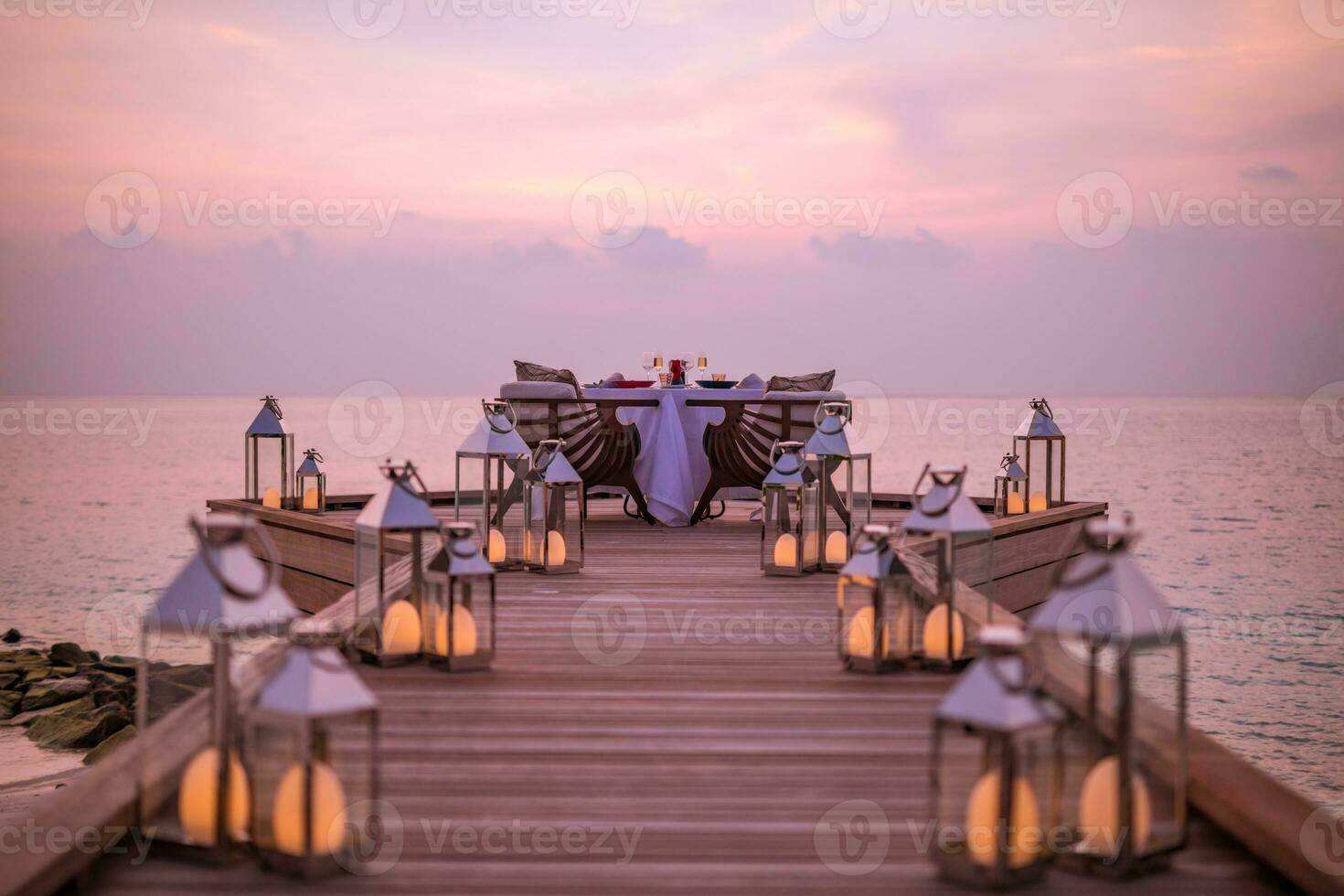Fantastisk romantisk middag på de strand på trä- däck ljus under solnedgång himmel. roman och kärlek, lyx destination middag, exotisk tabell uppstart med hav se. smekmånad förslag design foto