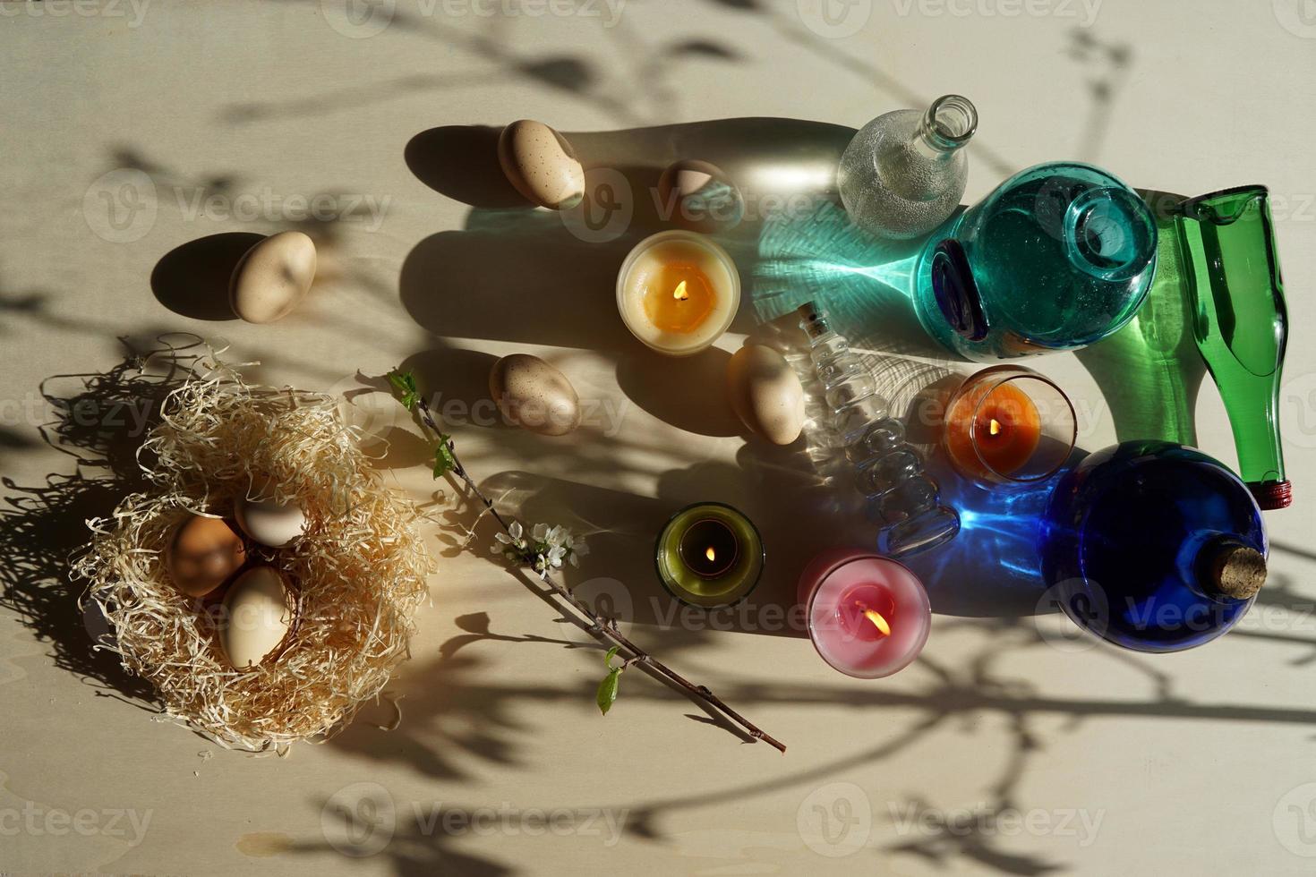 påskägg i halmboet och dekorativa färgglada glas med vatten på det gulvita bordet. foto