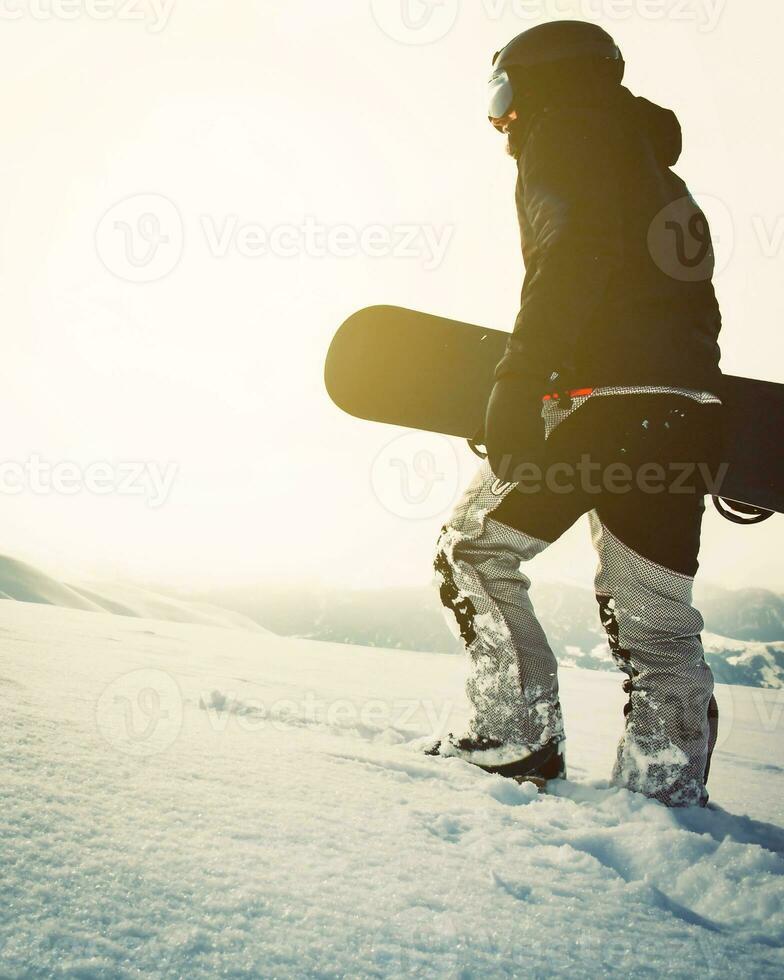snowboardåkare gående med snowboard under solnedgång i de snöig berg. filmiska solo- fripassagerare snowboardåkare bakgrund foto