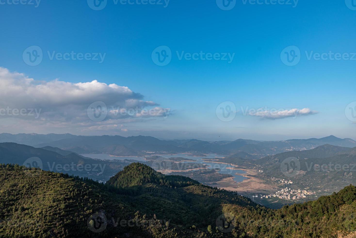 reservoaren under den blå himlen och de vita molnen omges av berg och skogar foto